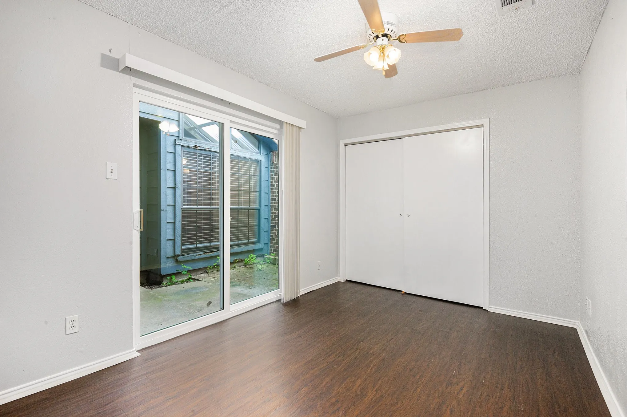 Wood-finish flooring throughout, sliding glass door, overhead ceiling fan, white bi-fold closet doors, and light neutral wall paint