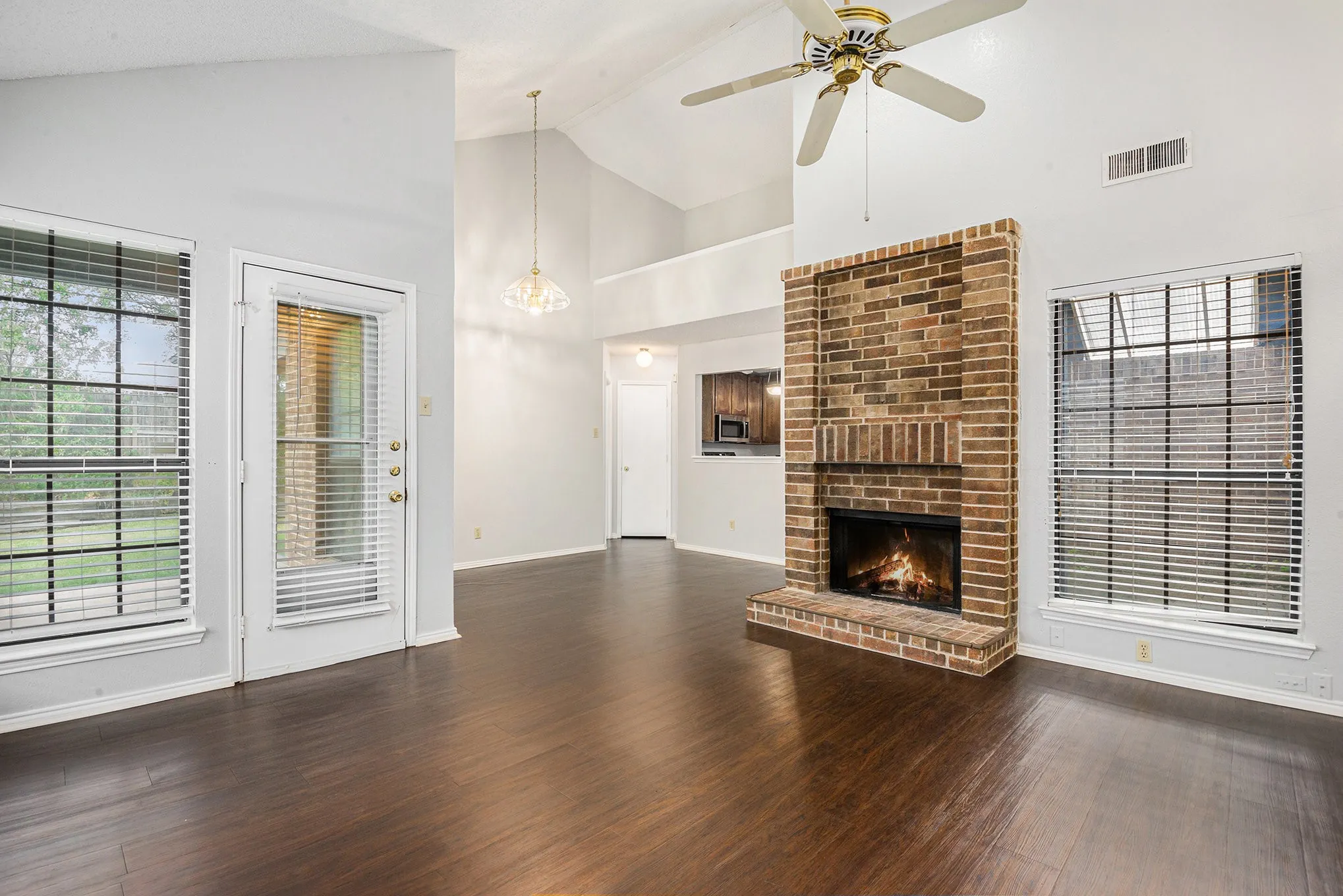 Vaulted ceiling with a ceiling fan, brick fireplace, wood-finish flooring, and multiple large windows