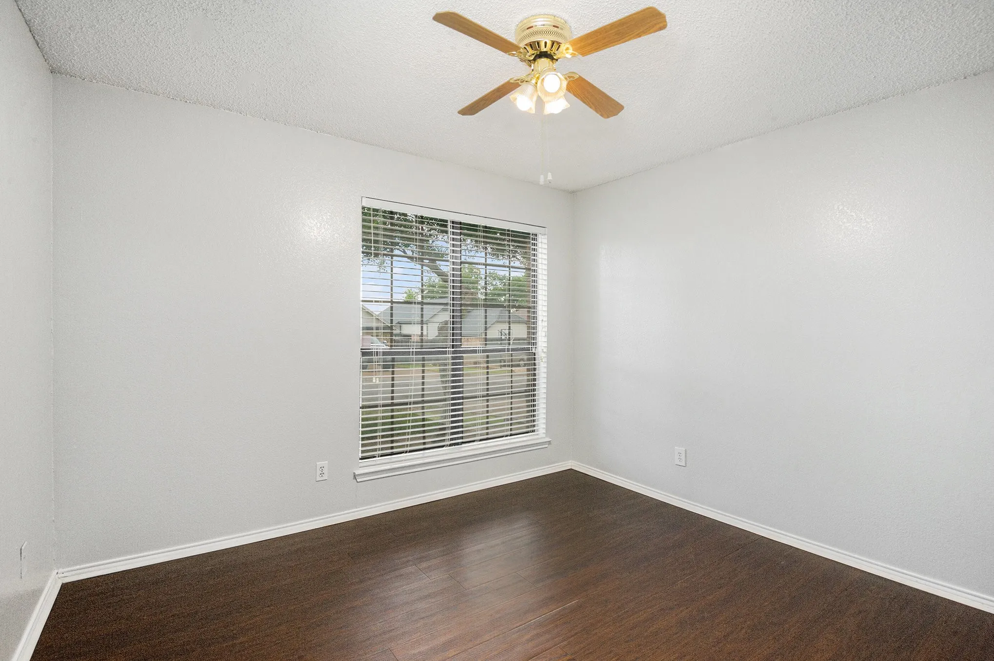 Wood-finish flooring, ceiling fan with integrated lighting, window with blinds, and white trim