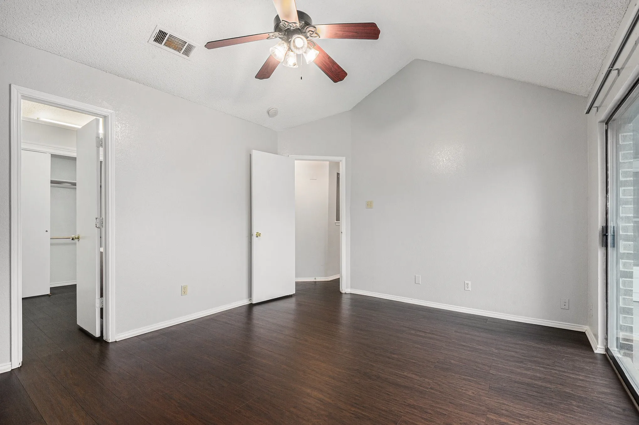 Vaulted ceiling with a ceiling fan, dark wood-finish flooring, sliding glass door, and white walls
