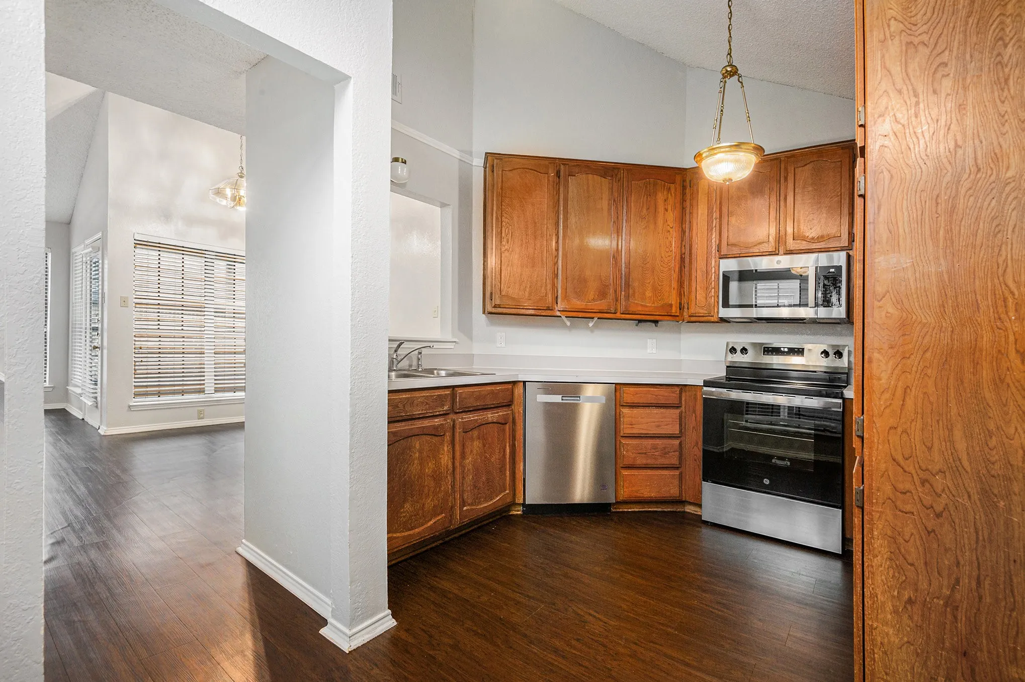 Kitchen featuring wood-finish flooring, wood cabinetry, stainless steel appliances, and a vaulted ceiling