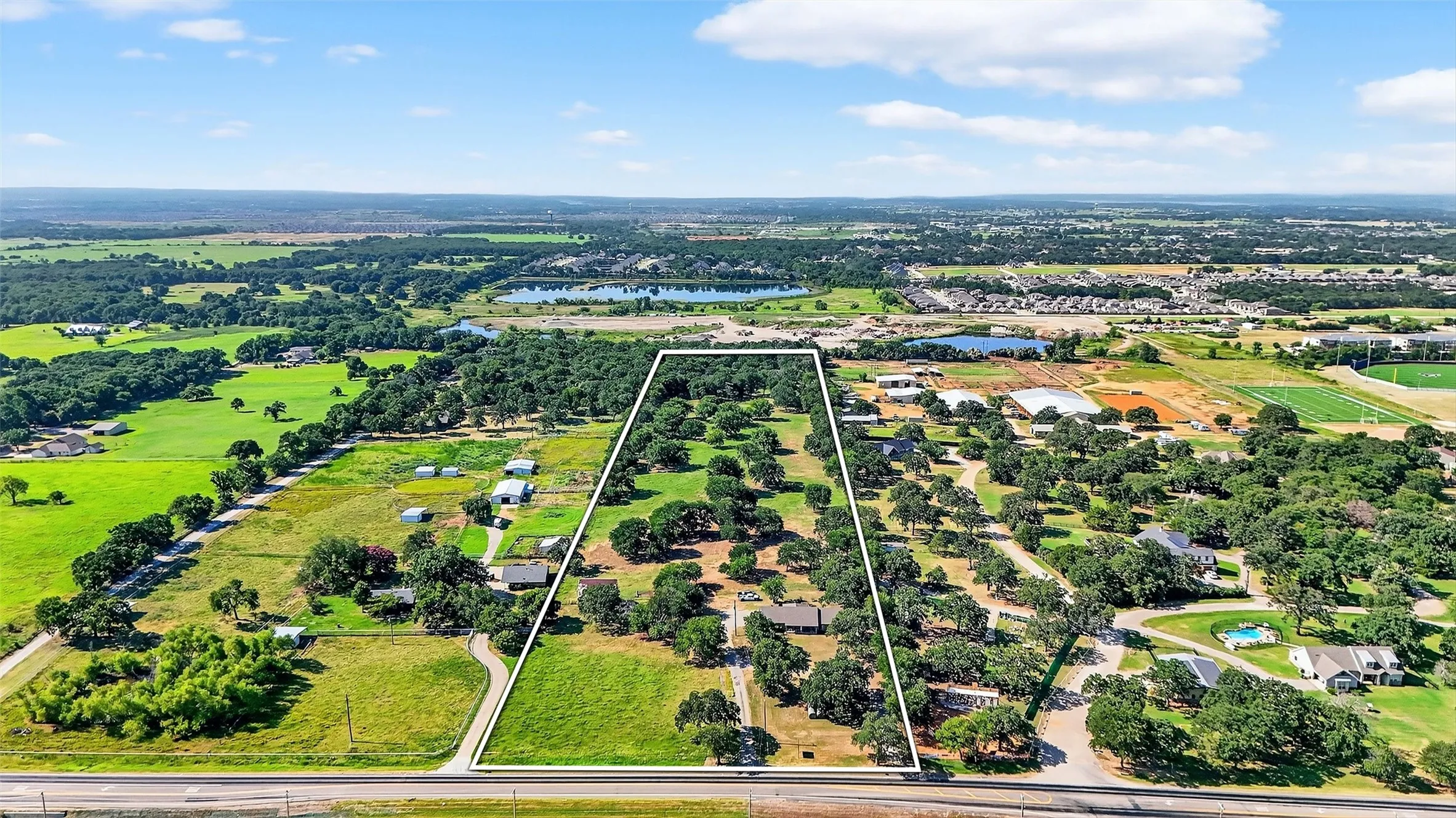 Expansive property featuring a treed landscape, multiple structures, and a paved road frontage