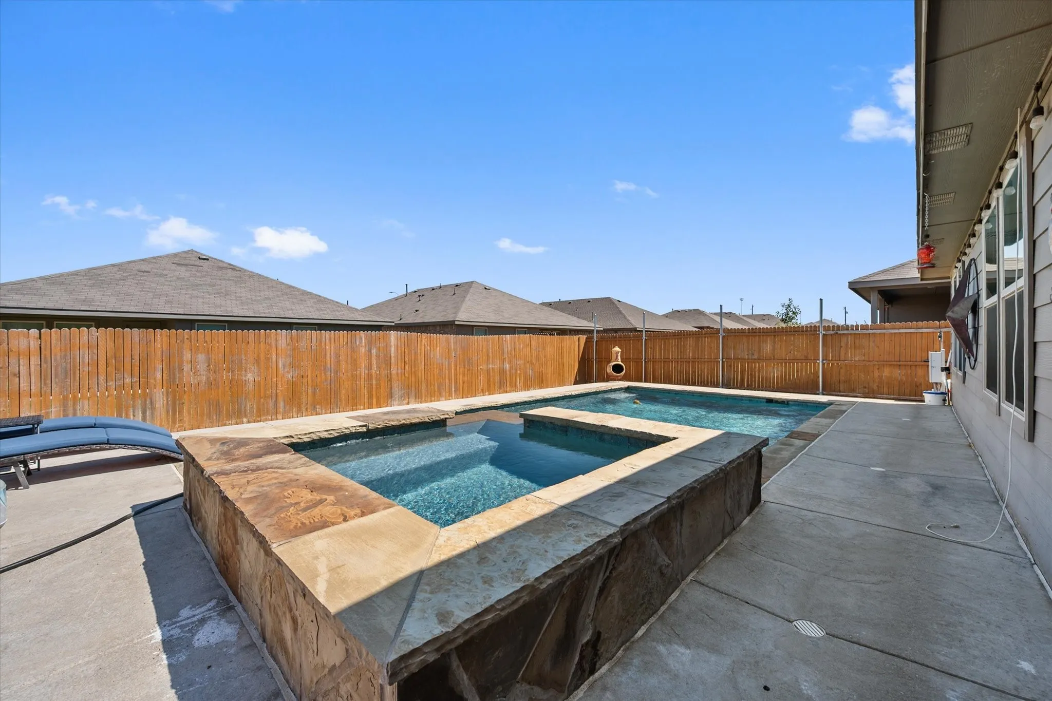 Backyard features a built-in pool and spa, stone-clad pool surround, and concrete patio