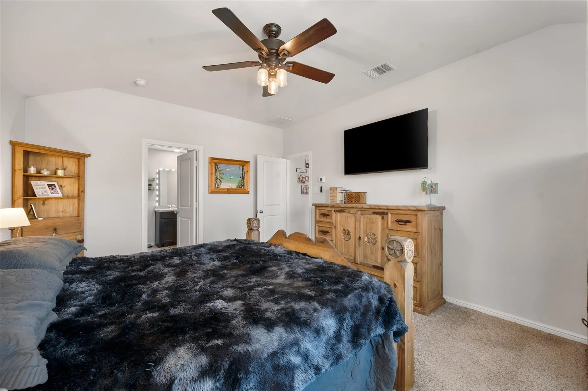 Vaulted ceiling with a ceiling fan, light neutral walls, carpet flooring, built-in shelving, and a door leading to a bathroom
