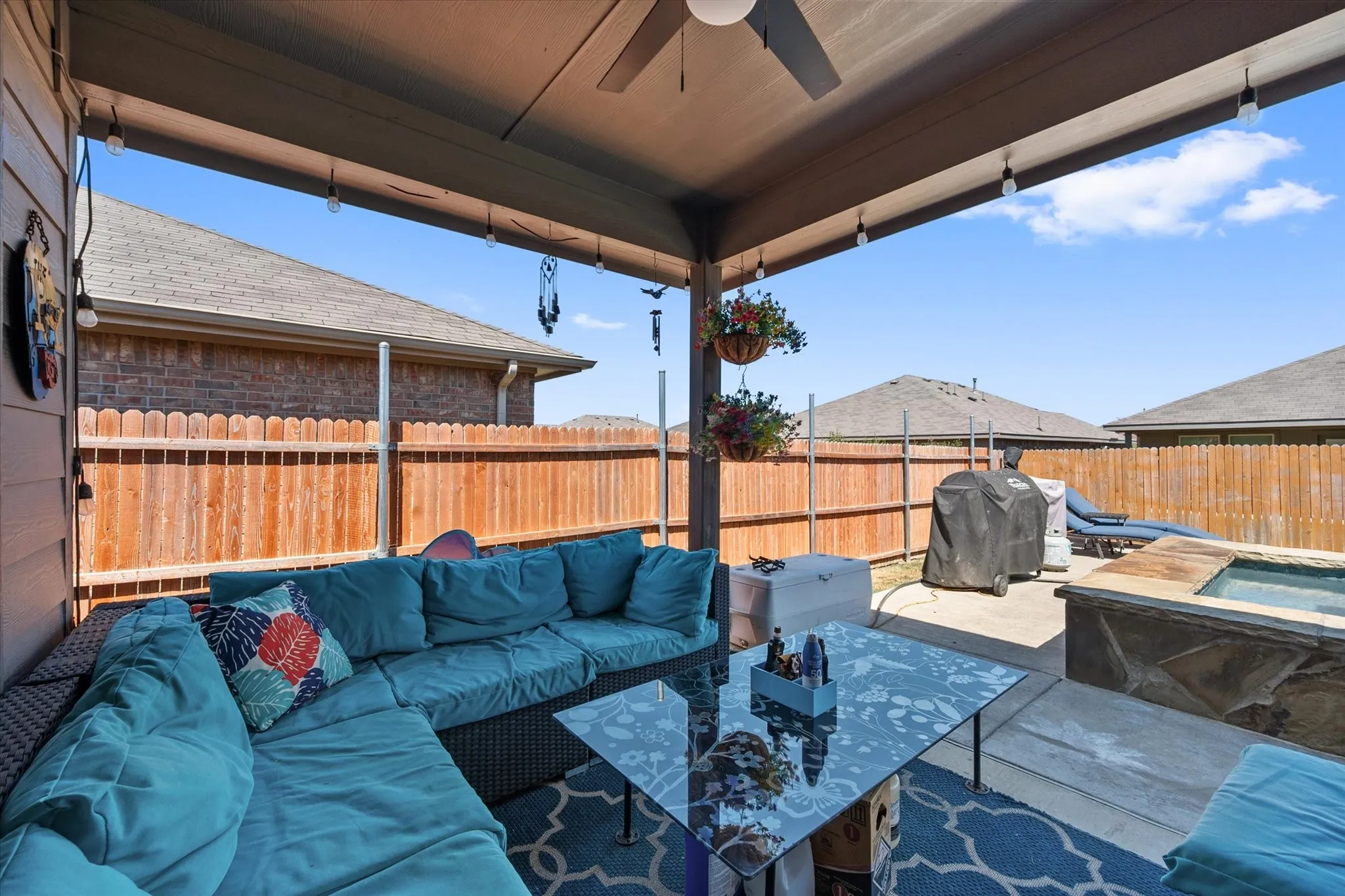 Covered patio featuring a ceiling fan, string lighting, privacy fencing, and an integrated spa