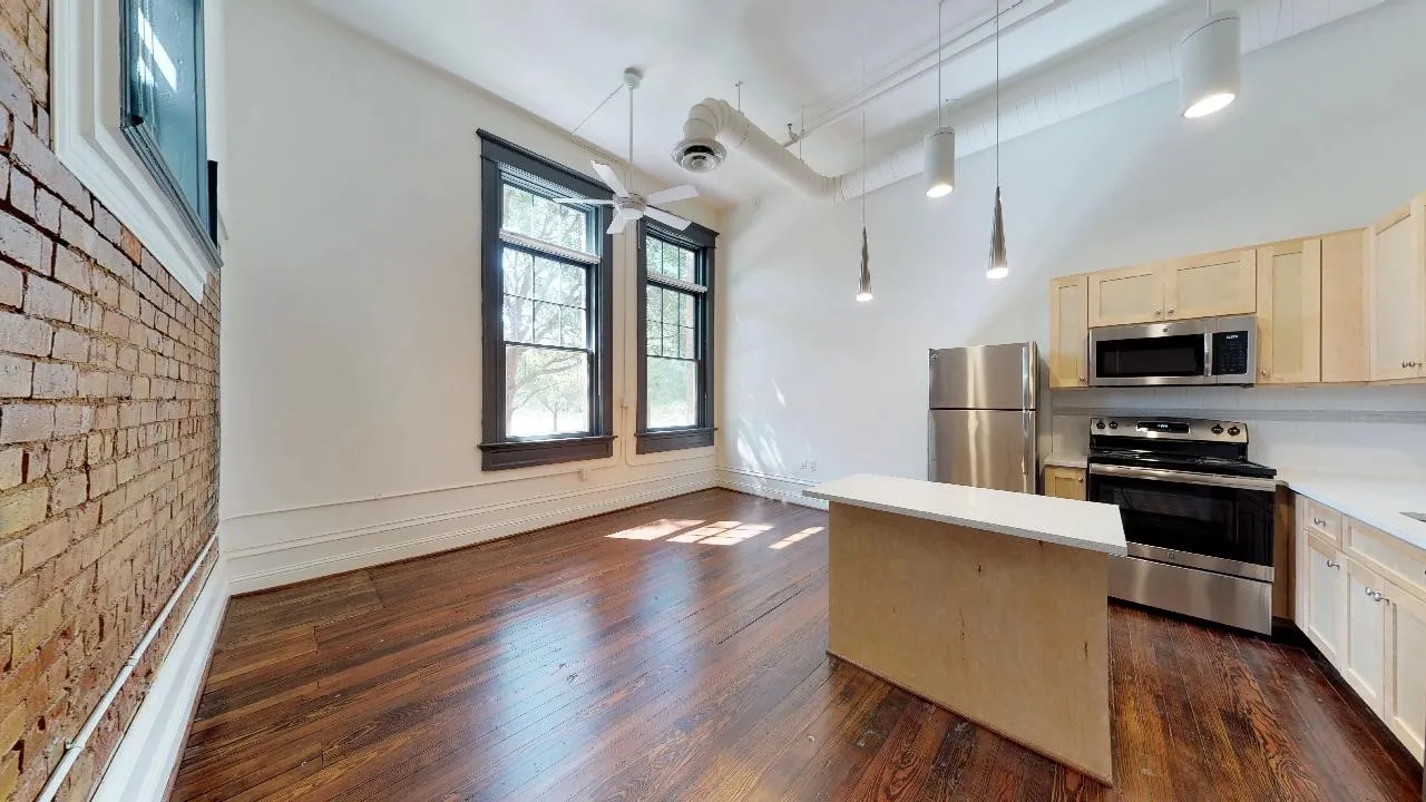 Kitchen featuring decorative light fixtures, dark hardwood / wood-style flooring, brick wall, and appliances with stainless steel finishes
