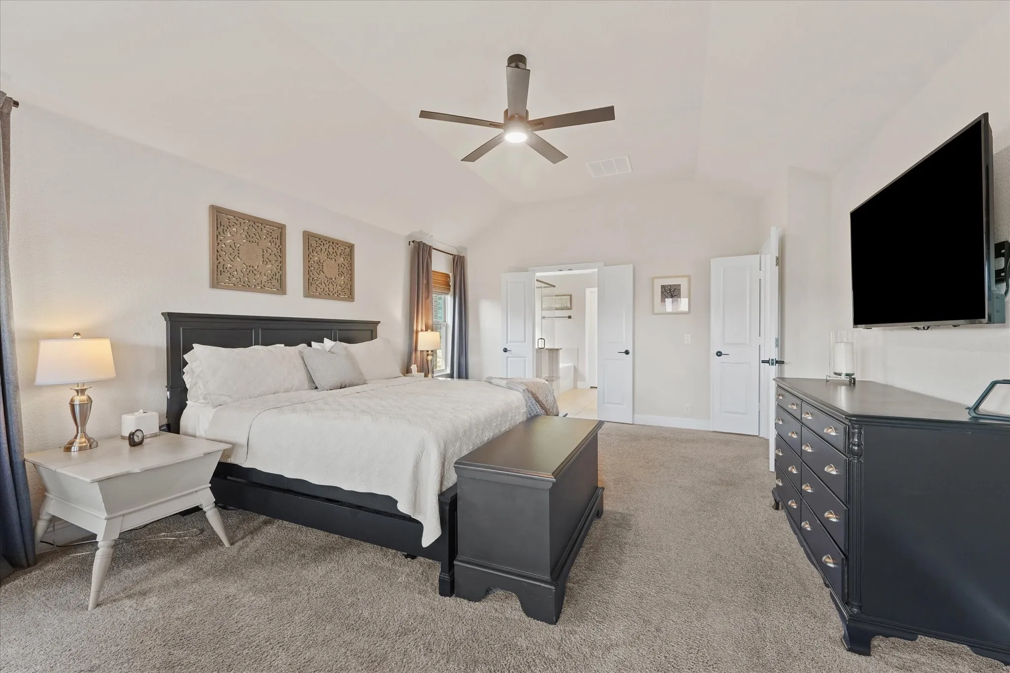Another view of the oversized primary bedroom showing the vaulted ceiling, generous floor space, and direct access to the ensuite bathroom.