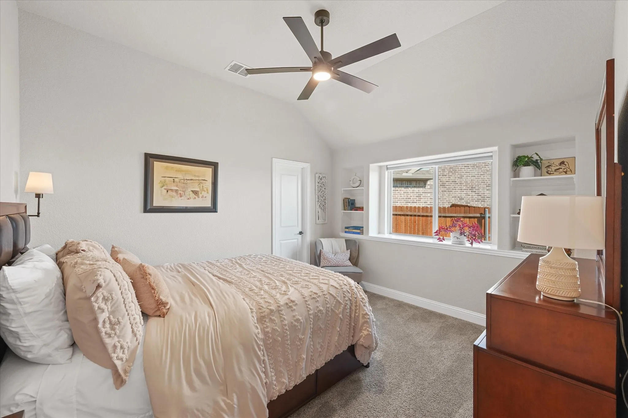 First-floor primary bedroom with vaulted ceiling, large windows, built-in shelving, ceiling fan, and space for a king-size bed in this 4-bedroom Country Lakes home near Argyle, TX.