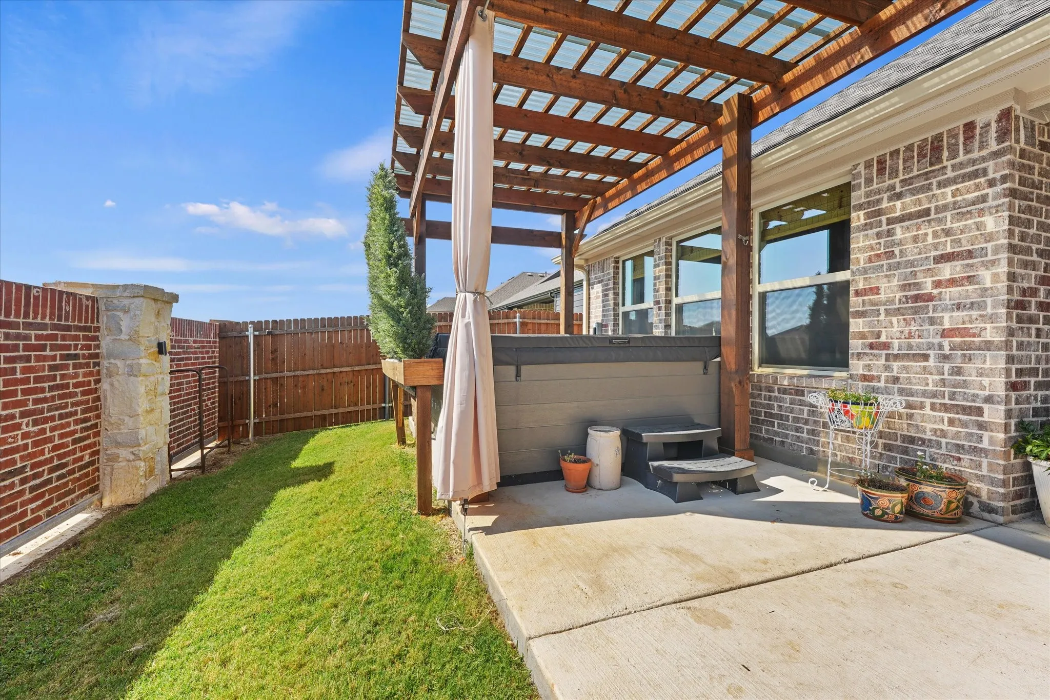 Backyard patio with a large wood pergola providing a defined outdoor living area. This angle also shows the additional yard space beside the patio.