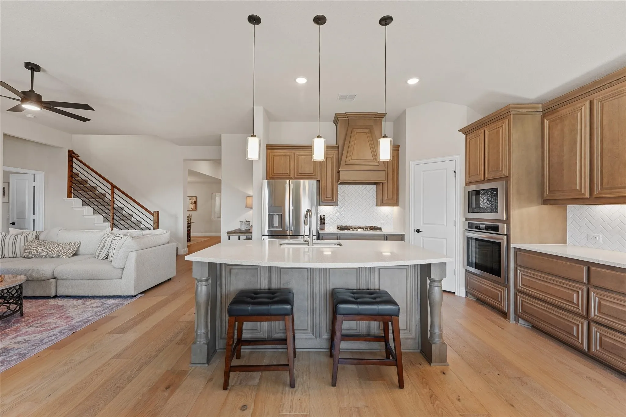 Open-concept kitchen with oversized quartz island, pendant lighting, built-in stainless steel appliances, gas cooktop, custom-style cabinetry, and engineered hardwood floors opening directly to the family room.