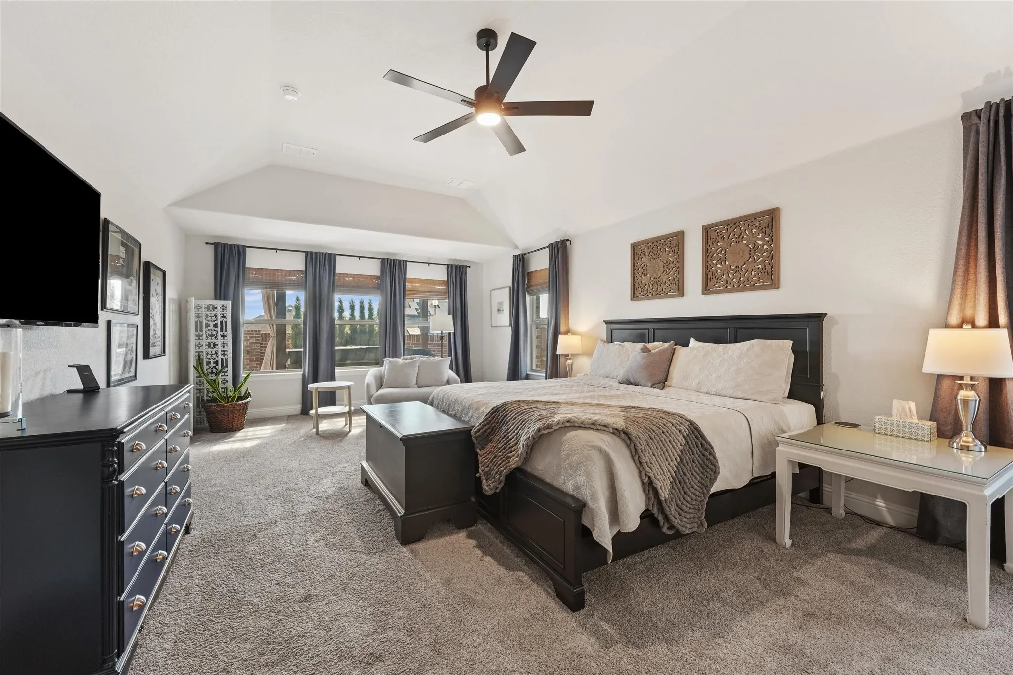 Spacious first-floor primary suite with vaulted ceiling, ceiling fan, multiple windows, and room for a king-size bed plus additional seating.
