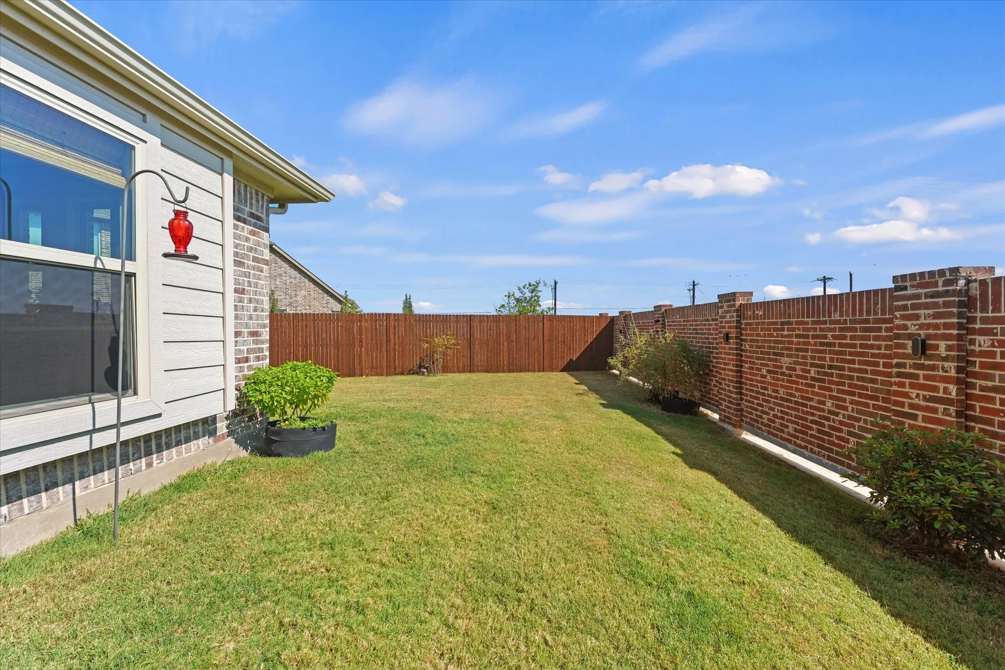 Fenced backyard with grassy lawn, established landscaping, brick privacy wall along one side, and room for pets, play, or outdoor living.