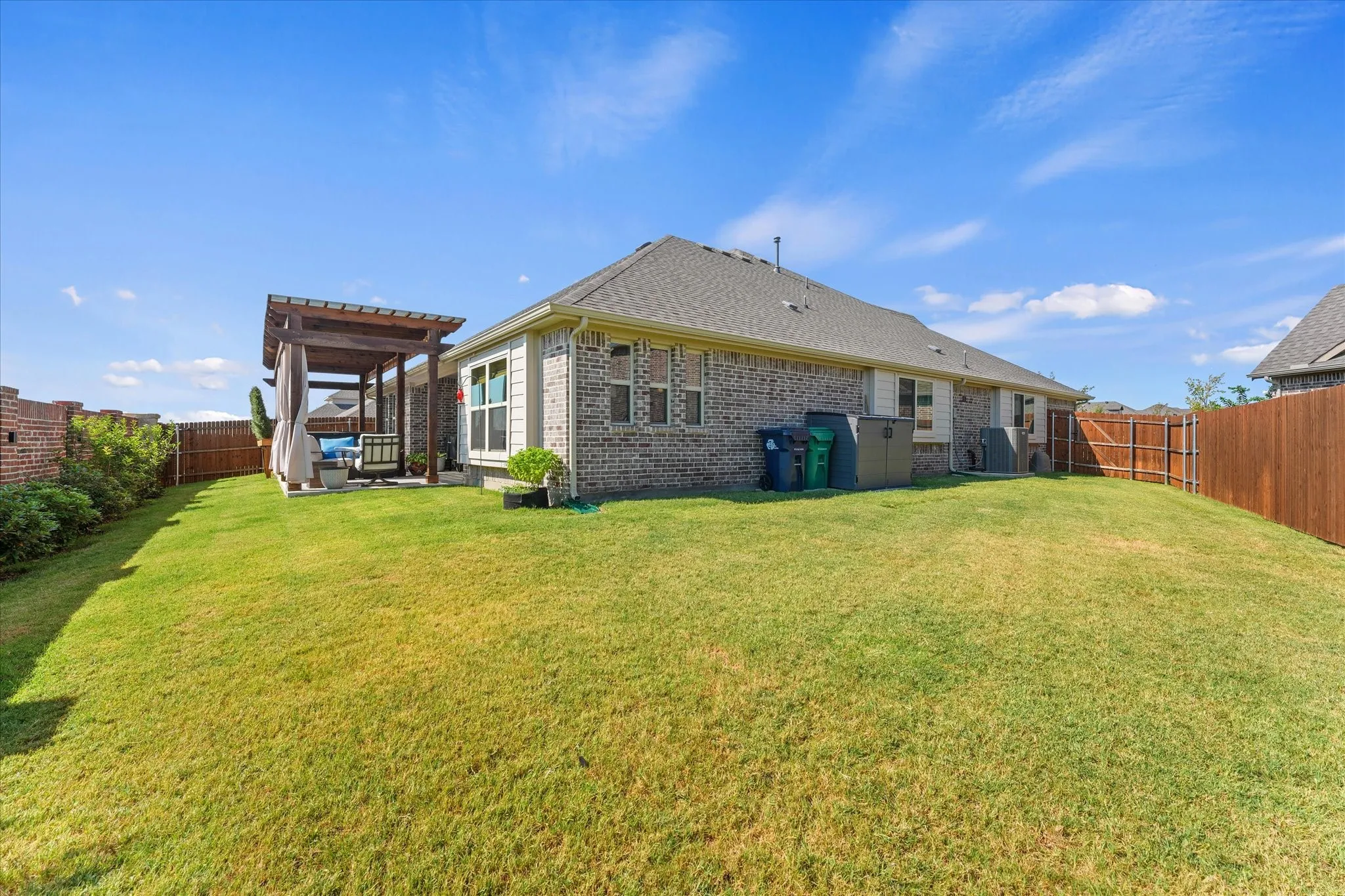 Wide view of the fenced backyard showing the amount of usable lawn space, established landscaping, brick privacy wall, and outdoor living area.