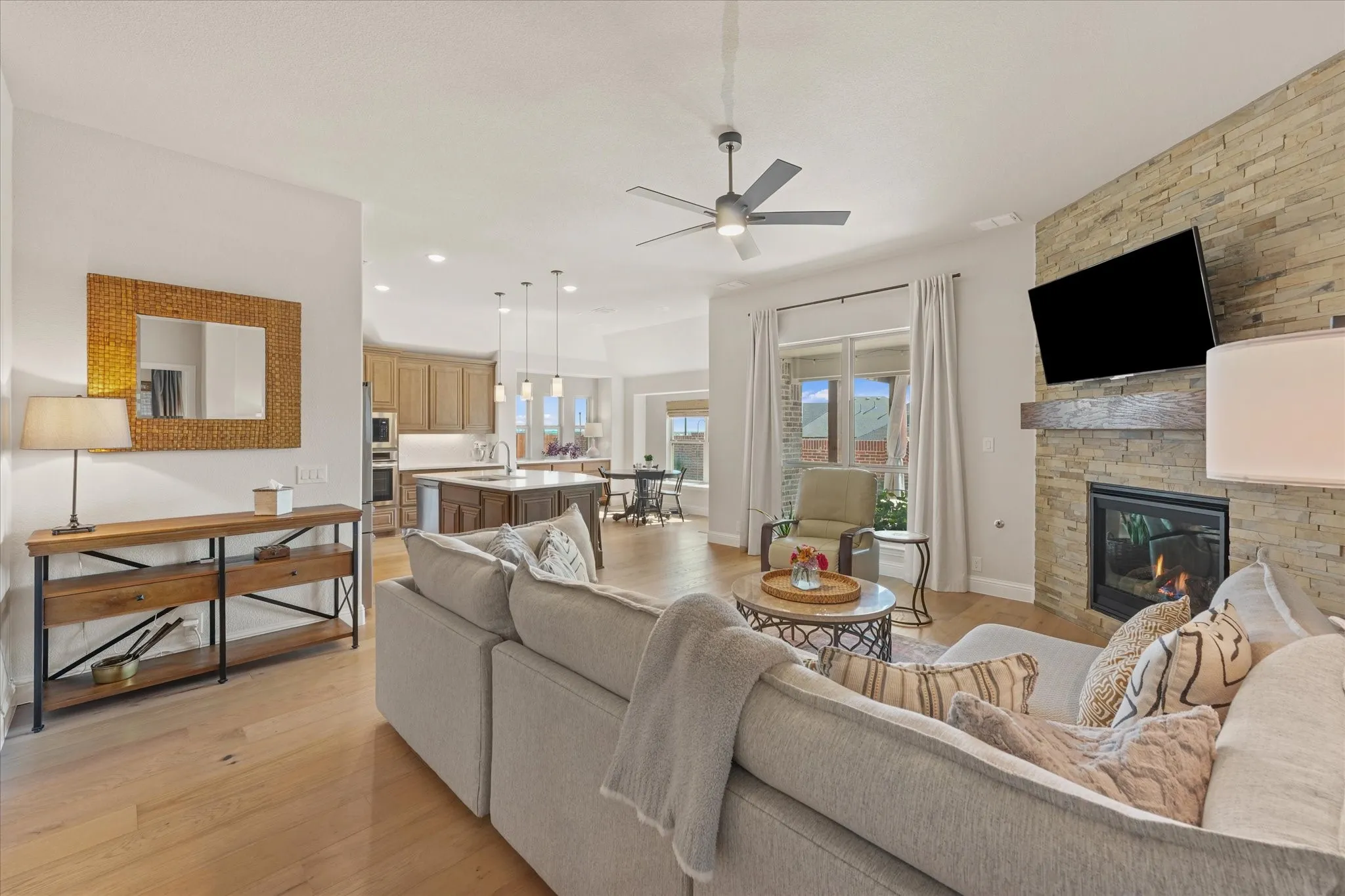 Open-concept living room connects directly to the kitchen and breakfast area with engineered hardwood floors, large windows, stone fireplace, and access to the covered back patio.