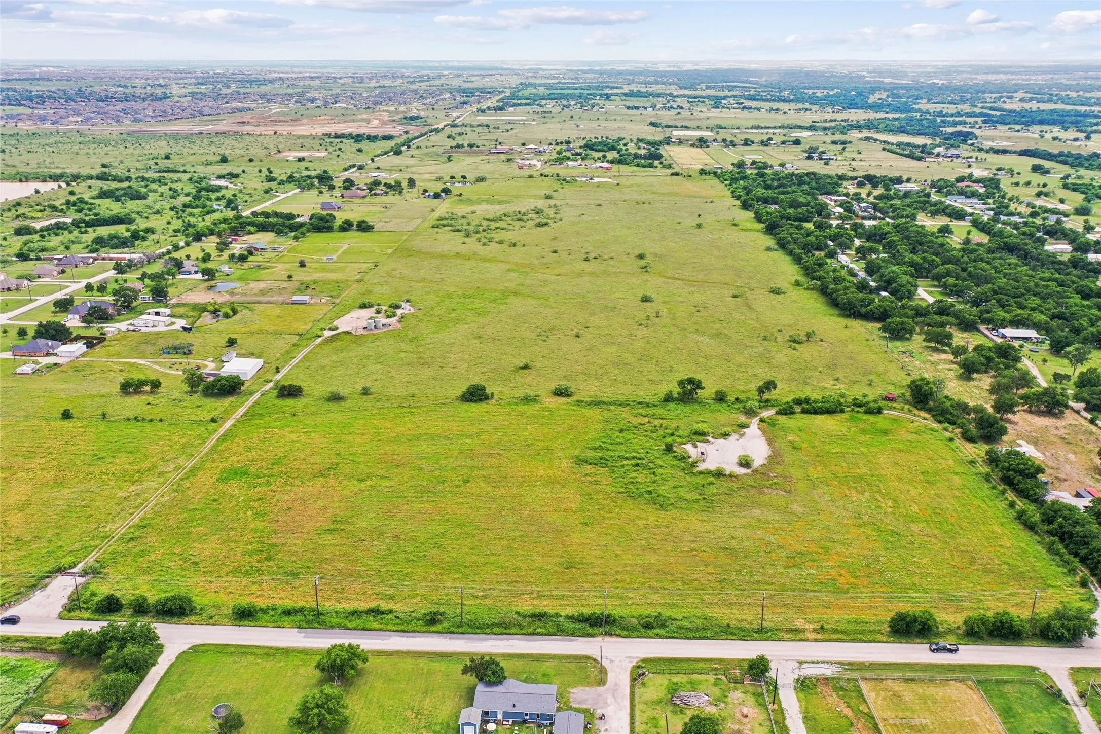 Expansive open land featuring a clear perimeter, established road frontage, and distant residential developments