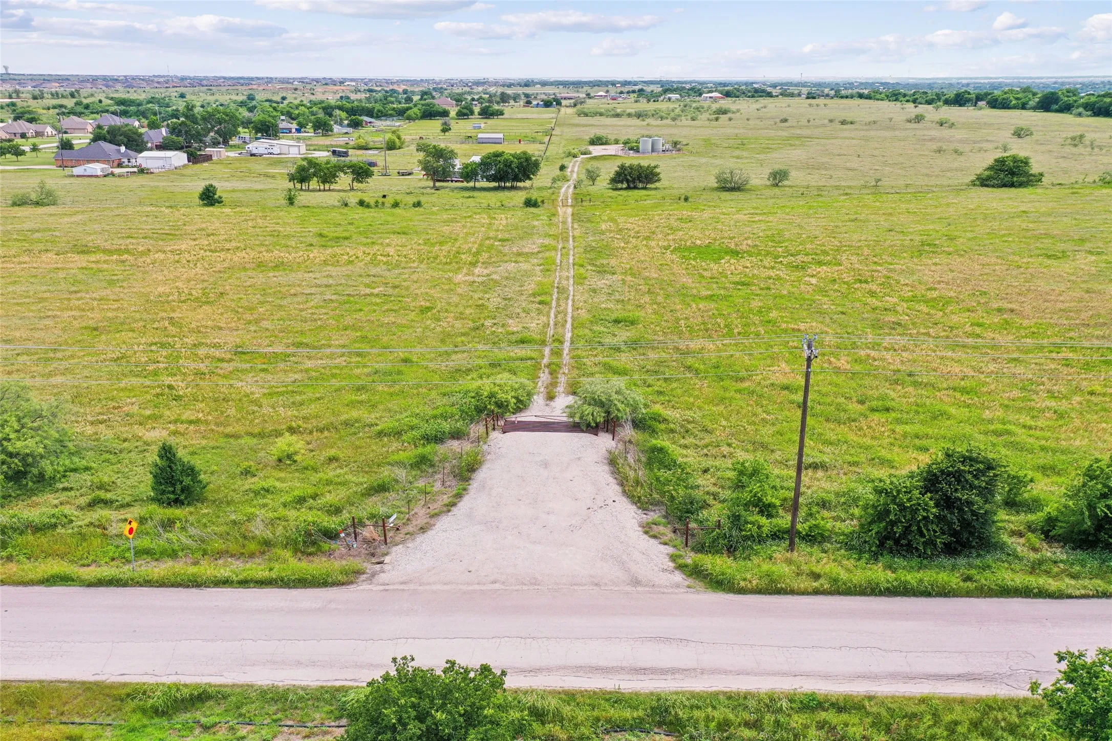 Expansive open field with a defined gravel entry, surrounding green landscape, and distant residential structures