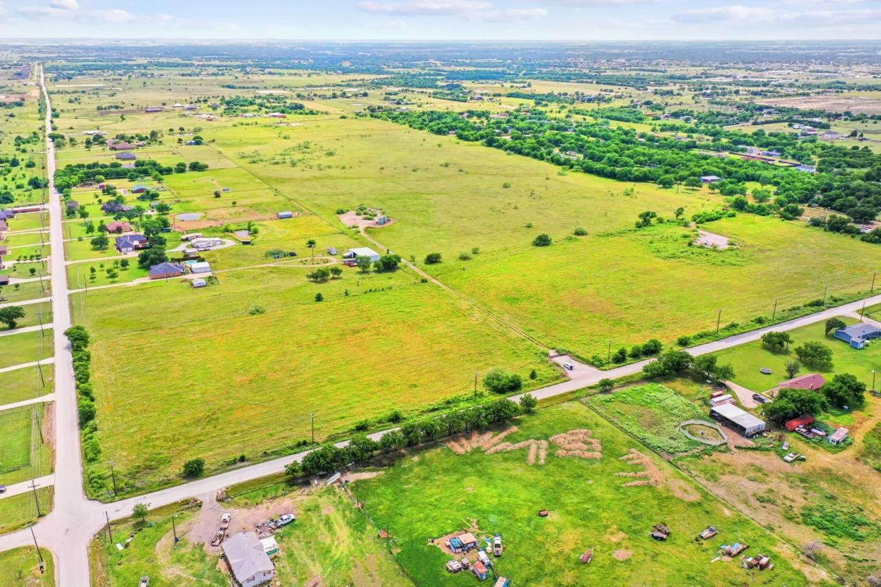 Expansive green acreage featuring multiple residential structures and paved road access
