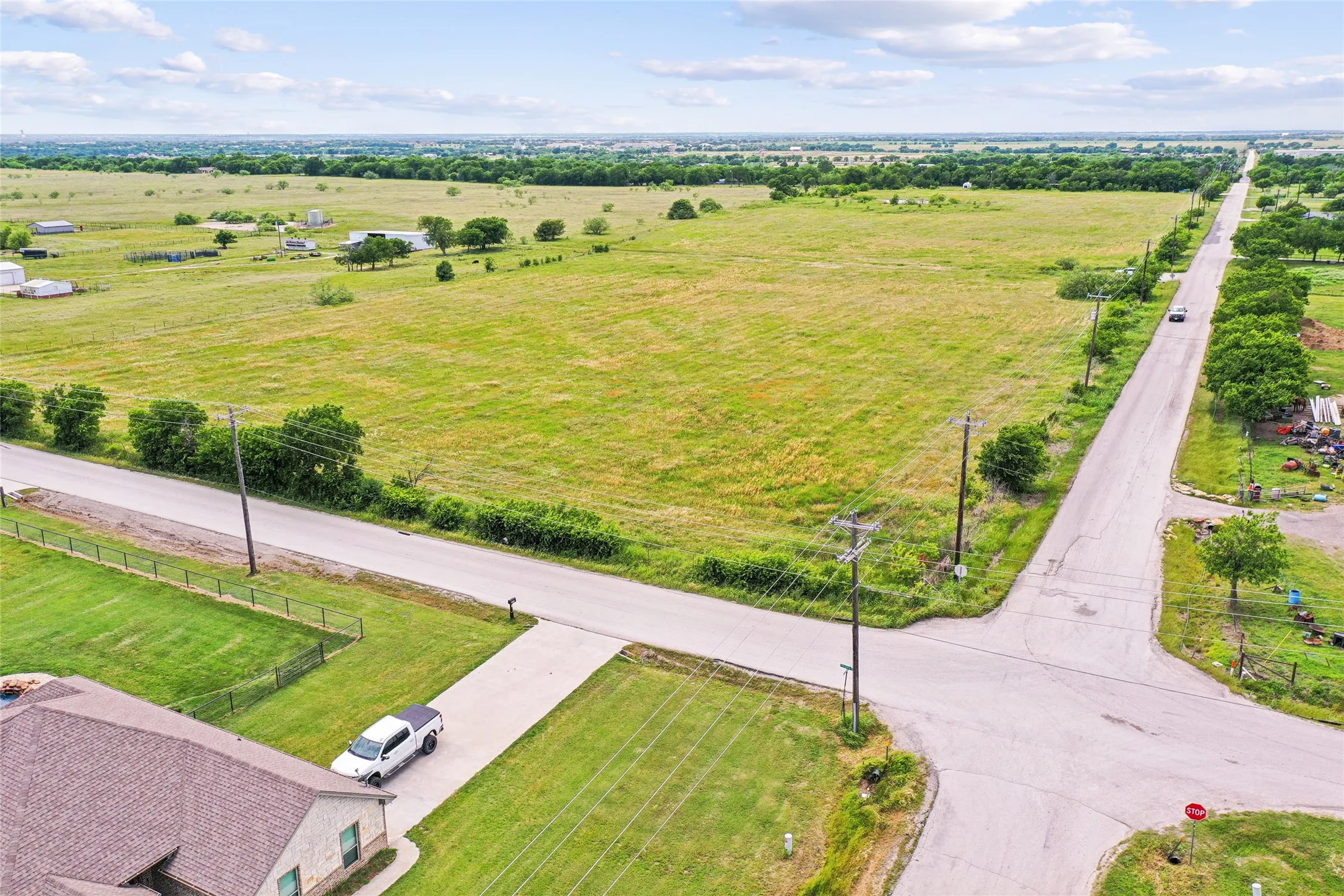 Expansive green landscape with distant structures, bordered by an asphalt road with power lines
