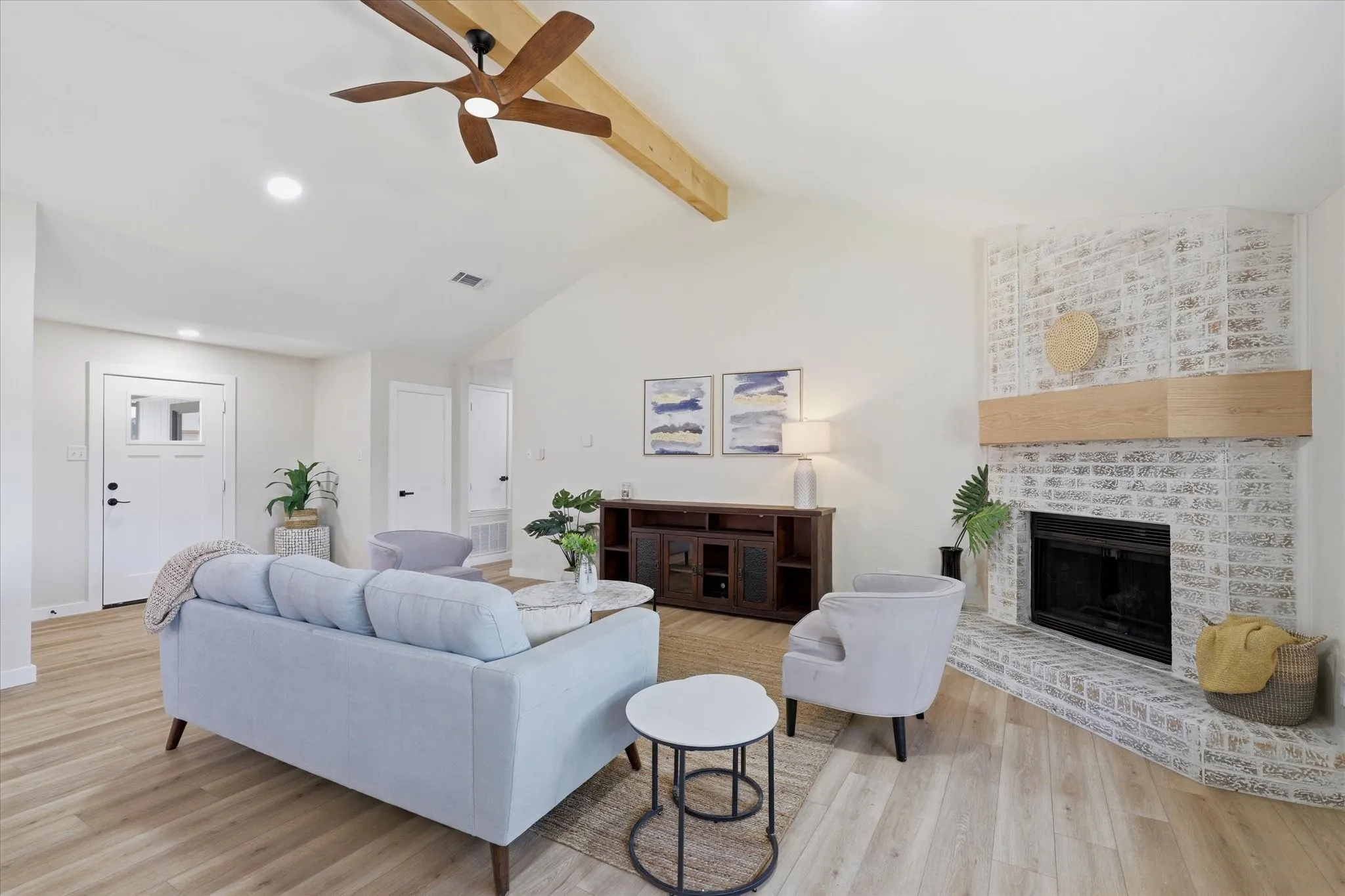 Vaulted ceiling with wood beam accent, wood-finish flooring, recessed lighting, and a whitewashed brick fireplace with a wood mantle