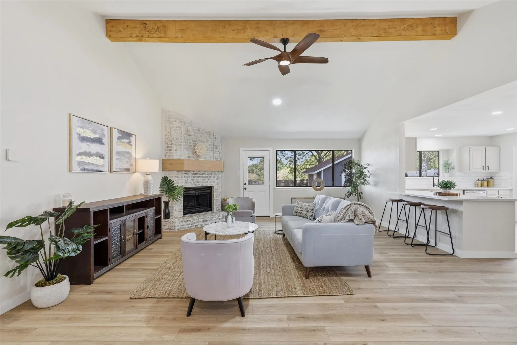 Vaulted ceiling with exposed wood beam, wood-finish flooring, brick fireplace with wood mantel, built-in kitchen island with seating, and recessed lighting