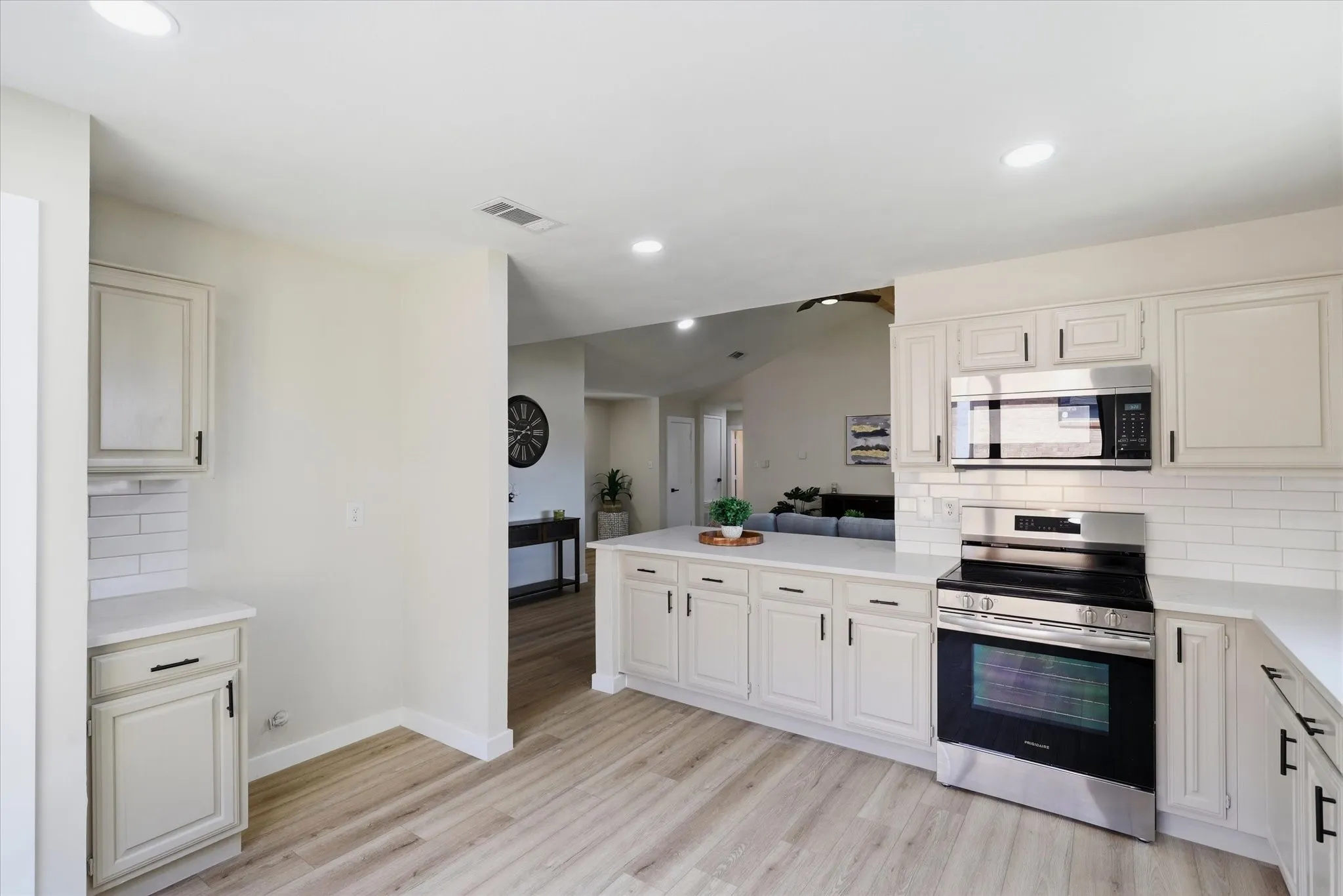 Modern kitchen featuring light wood-finish flooring, white cabinetry with black hardware, white subway tile backsplash, and recessed lighting