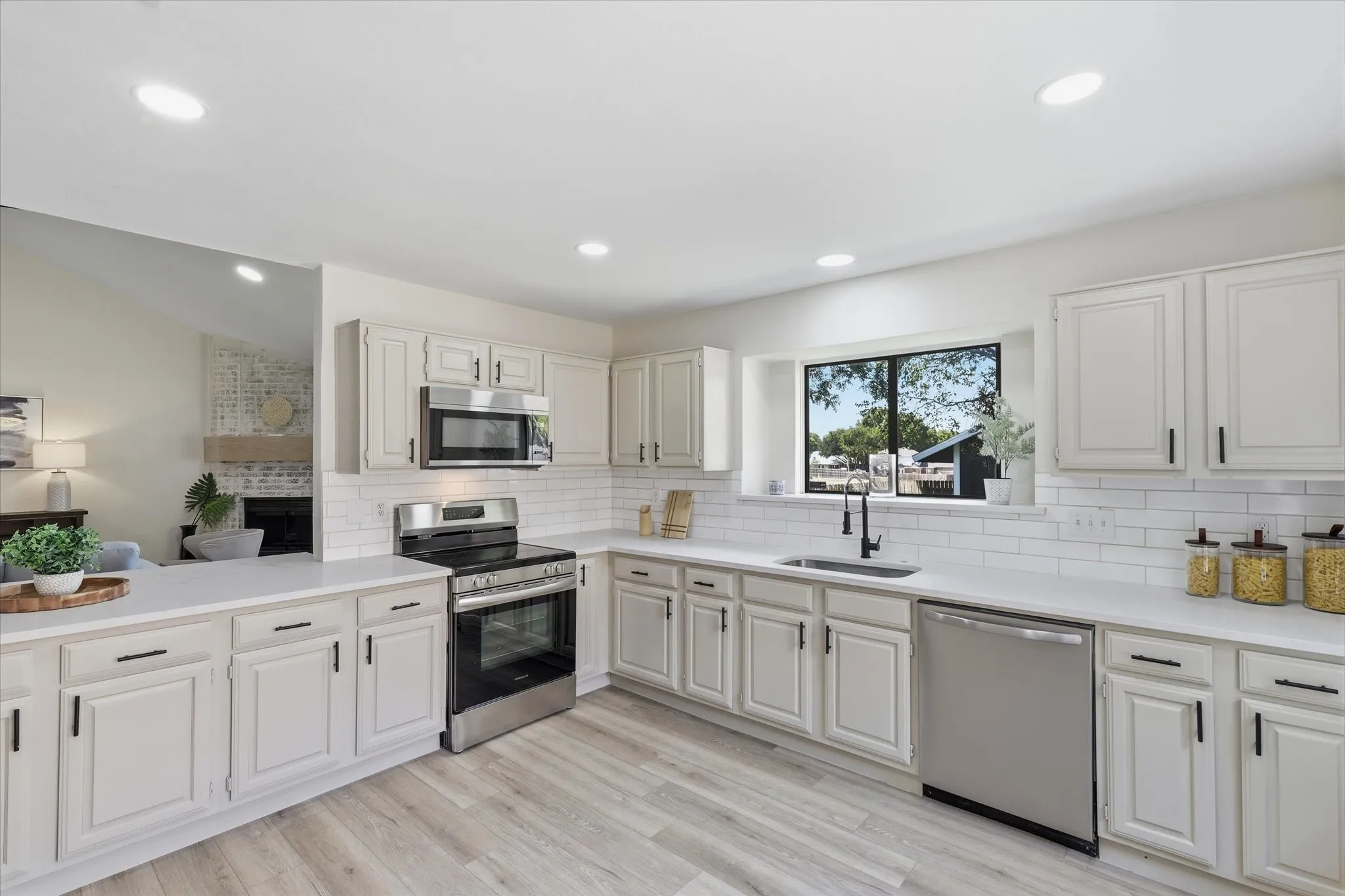 White shaker cabinetry, light wood-finish flooring, stainless steel appliances, recessed lighting, and a subway tile backsplash