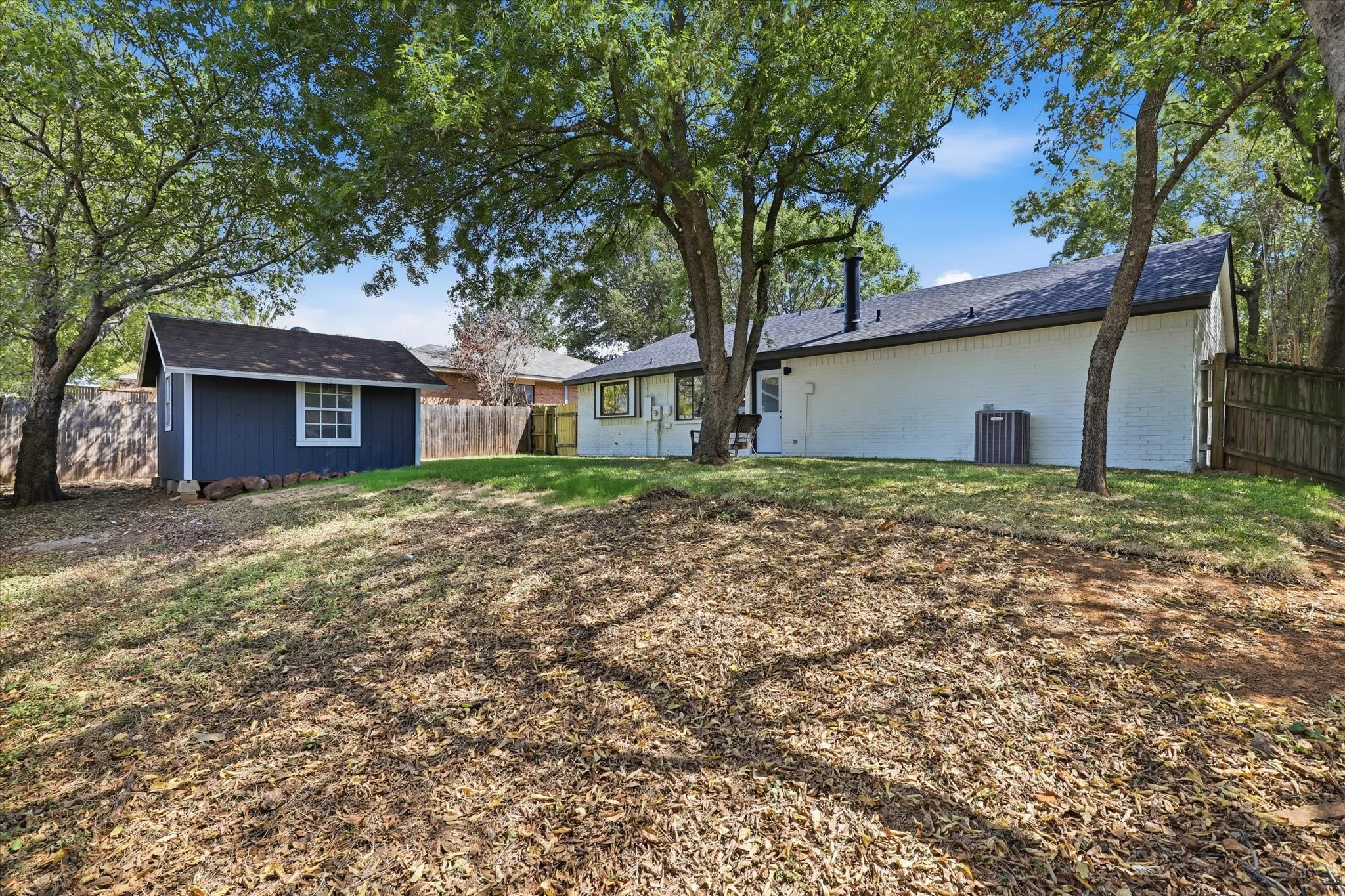 Expansive backyard featuring a detached storage shed, mature trees, and a private wooden fence
