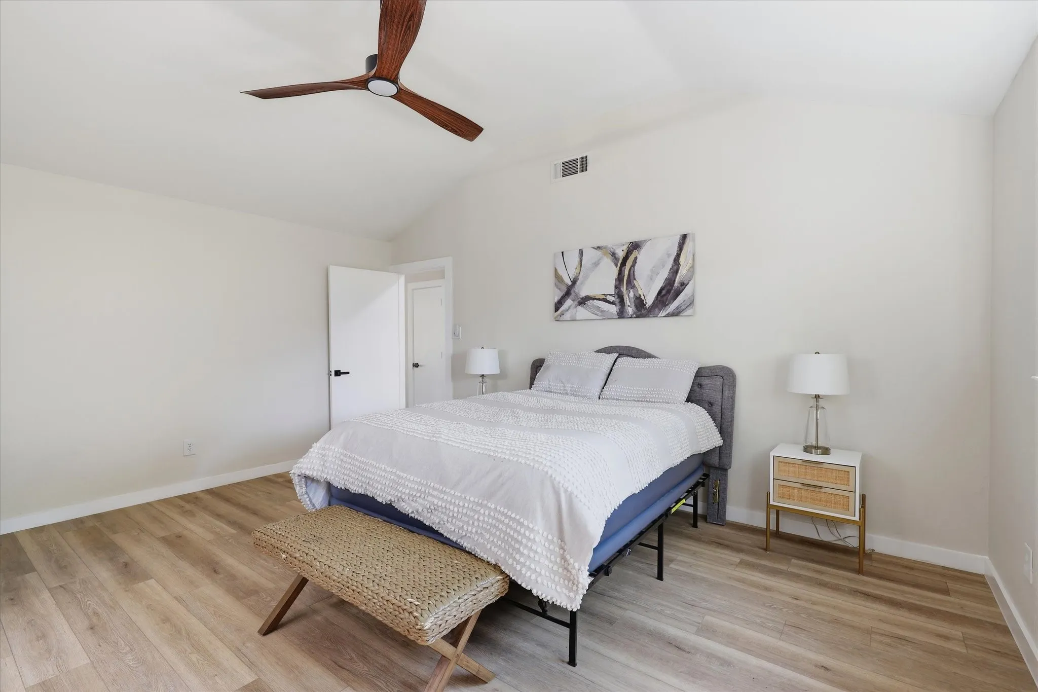 Vaulted ceiling, wood-finish flooring, modern ceiling fan, white paneled door, black door hardware