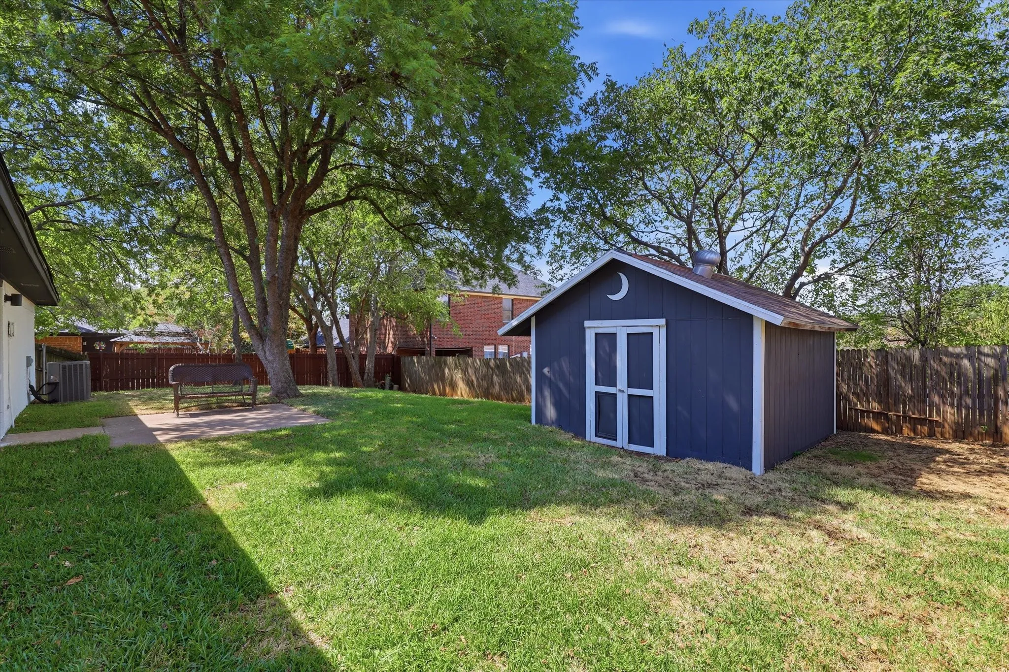 Expansive backyard with a manicured lawn, established trees, and a detached storage shed