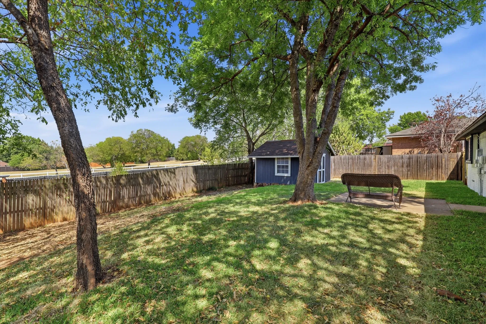 Expansive backyard oasis featuring mature shade trees, manicured lawn, and wooden privacy fencing