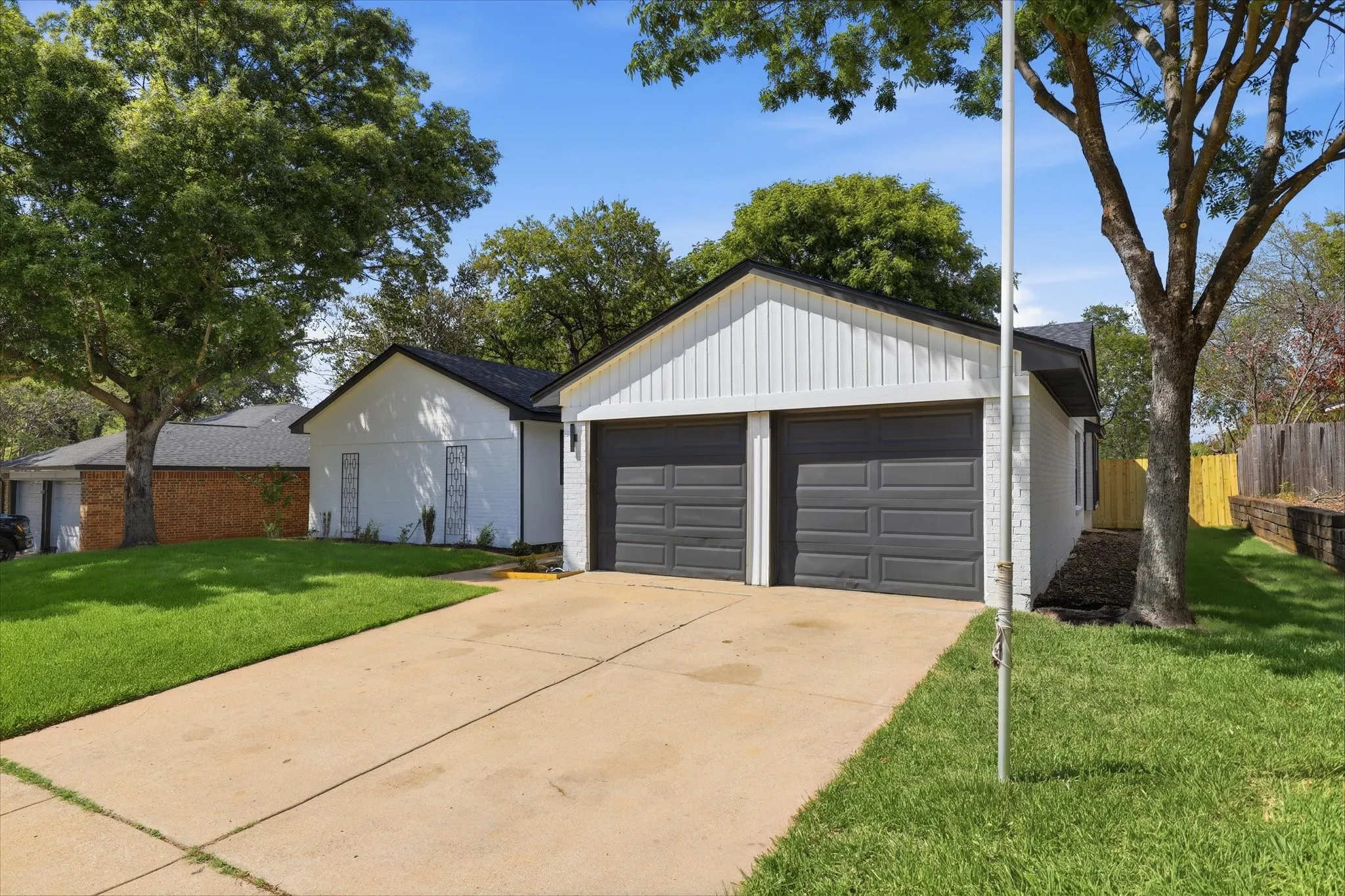 Two-car garage with dark paneled doors, light vertical siding, and a dark shingle roof