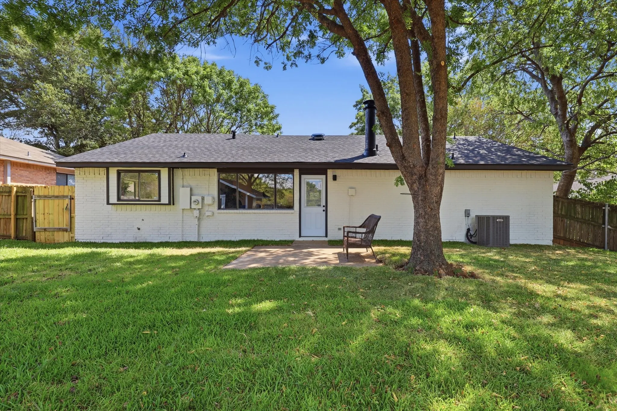 Expansive grassy backyard featuring a paved patio and mature trees