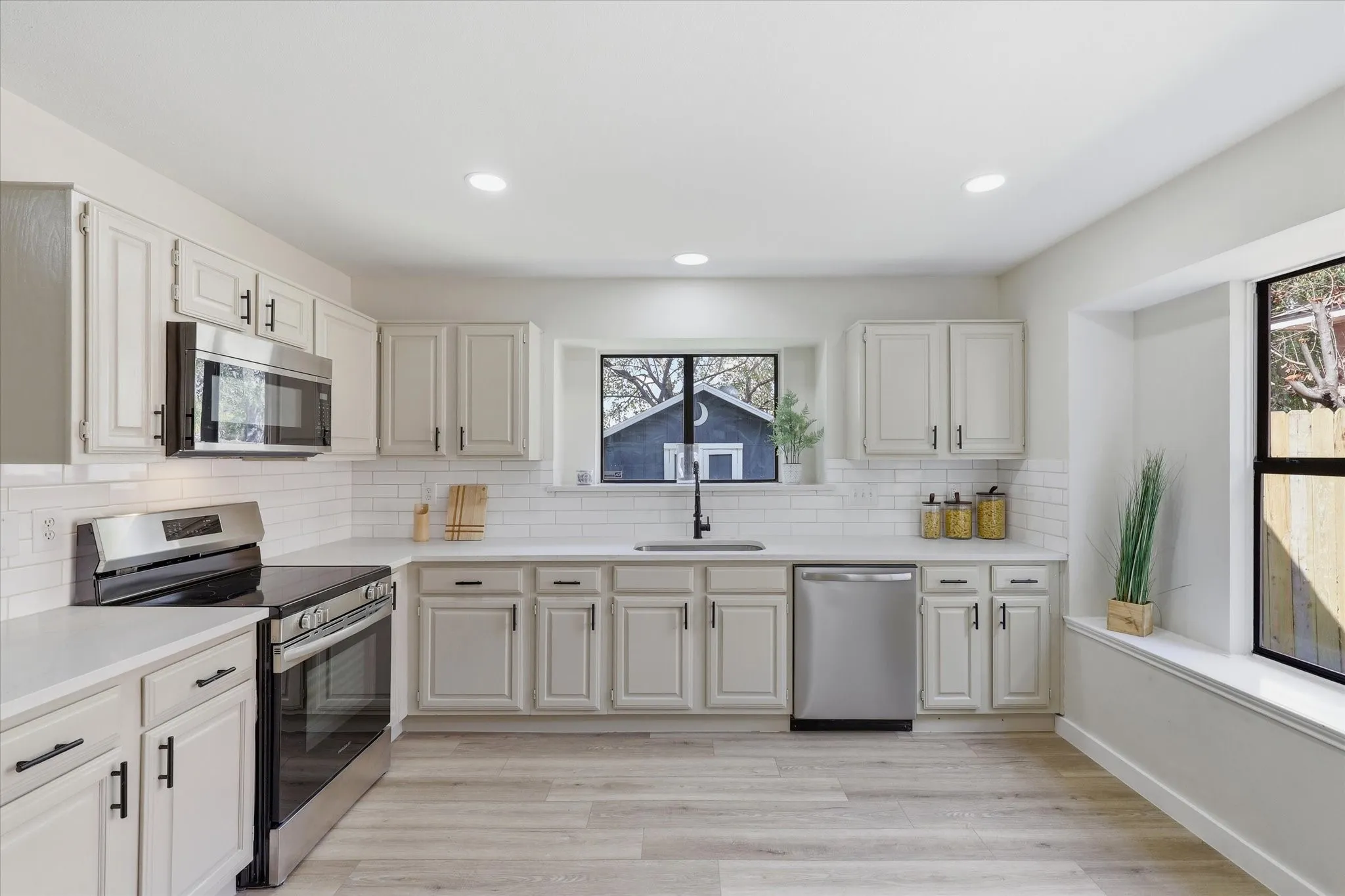 Contemporary kitchen featuring light wood-finish flooring, white cabinetry with black hardware, stainless steel appliances, and a white subway tile backsplash