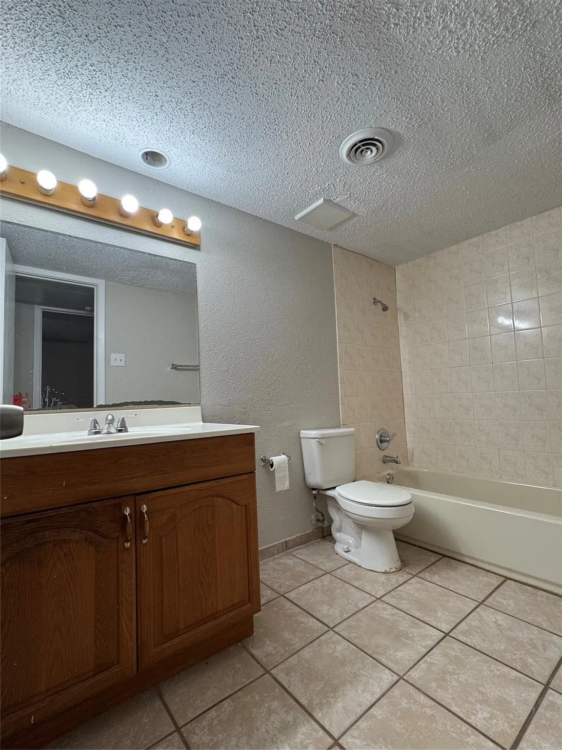 Tile flooring, integrated bathtub, tiled shower surround, wood-finish vanity, and a large wall mirror