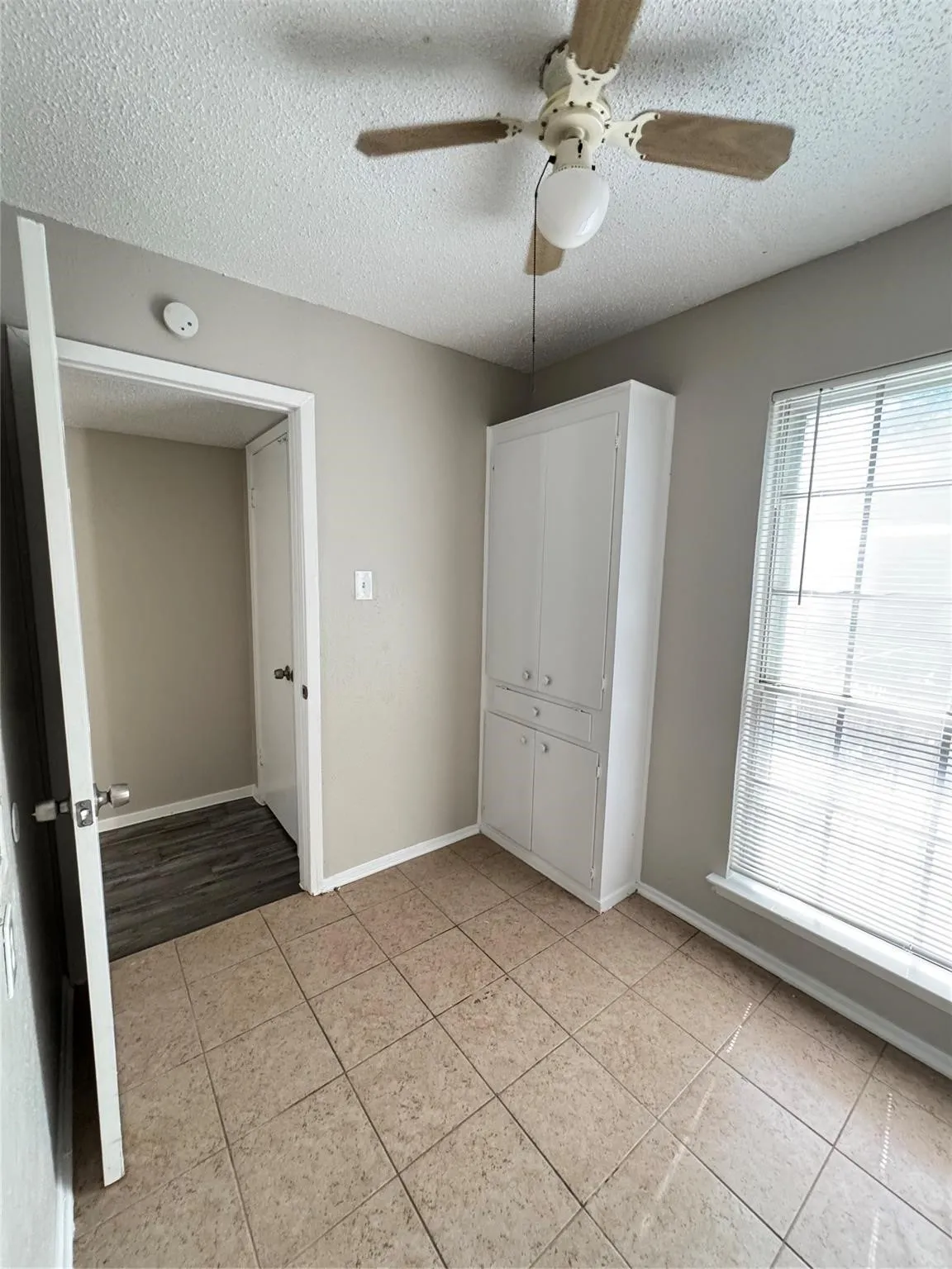 Built-in storage cabinet, tiled flooring, overhead ceiling fan with lighting, and window with horizontal blinds