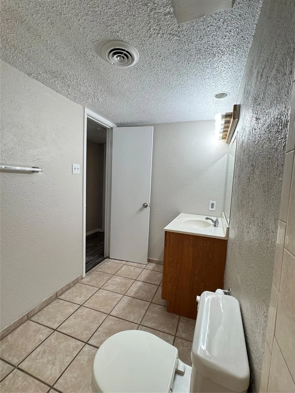Tiled flooring, single vanity with wood-finish cabinetry, and overhead lighting