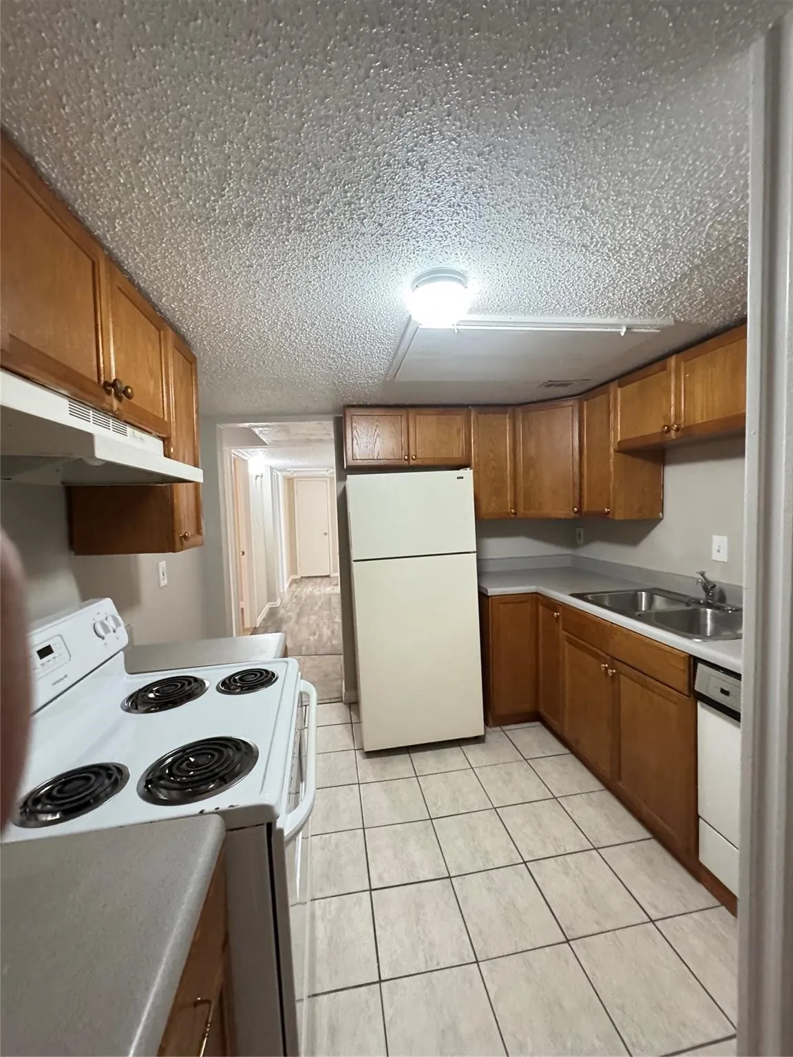 Galley kitchen featuring wood-finish cabinetry, tile flooring, and a double basin sink