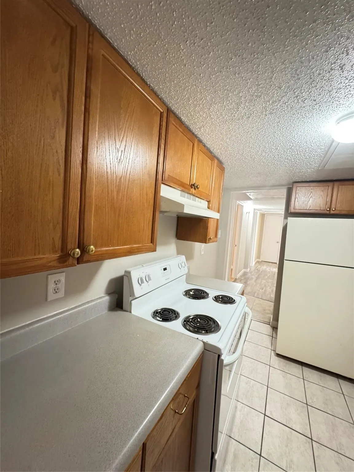 Wood-finish cabinetry, solid surface countertops, white electric range, white refrigerator, and tiled flooring