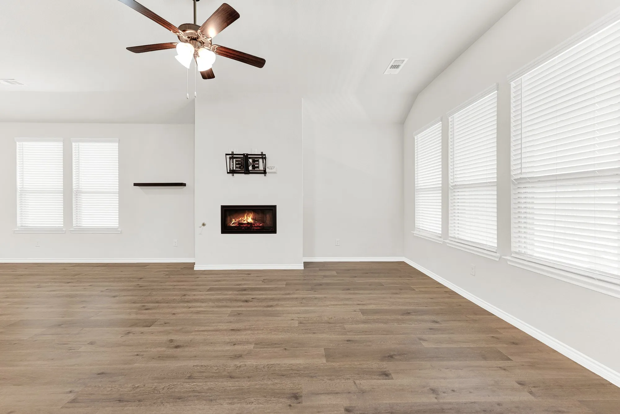 Abundant natural light streams through multiple large windows, emphasizing the stunning wood-look flooring and a modern, glowing fireplace as the room's warm focal point. This sanctuary is designed for comfort and effortless relaxation, offering a perfect, sunny spot to unwind.