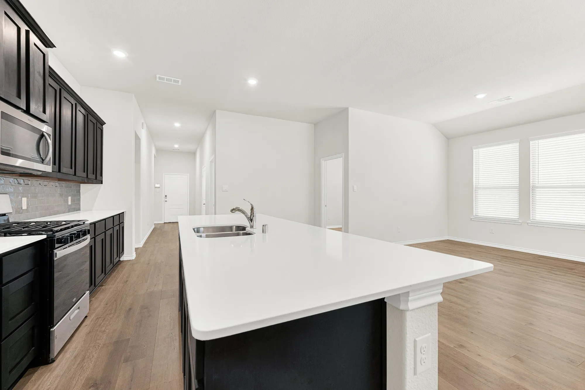 This kitchen's prominent white island features a seamless quartz countertop with an under-mount sink and a gooseneck faucet. You can easily prep meals while staying connected to your family or guests in the open living space