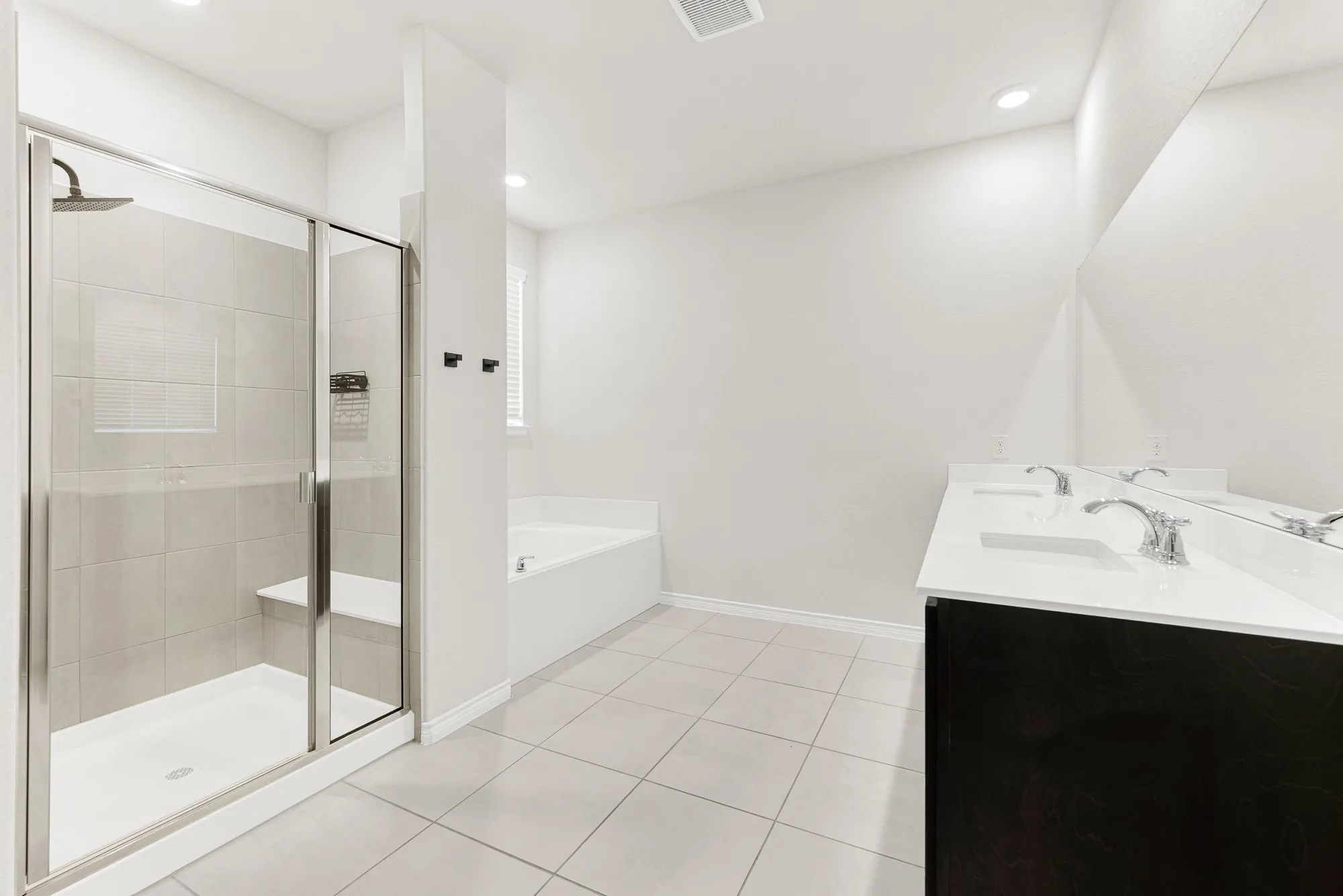 The spacious primary ensuite is revealed in this photo, highlighting the long double-sink vanity with dark cabinetry, large mirror, and separate glass-enclosed tile shower. Start your mornings refreshed or prepare for the day side-by-side in this thoughtfully designed, upscale spa bathroom.