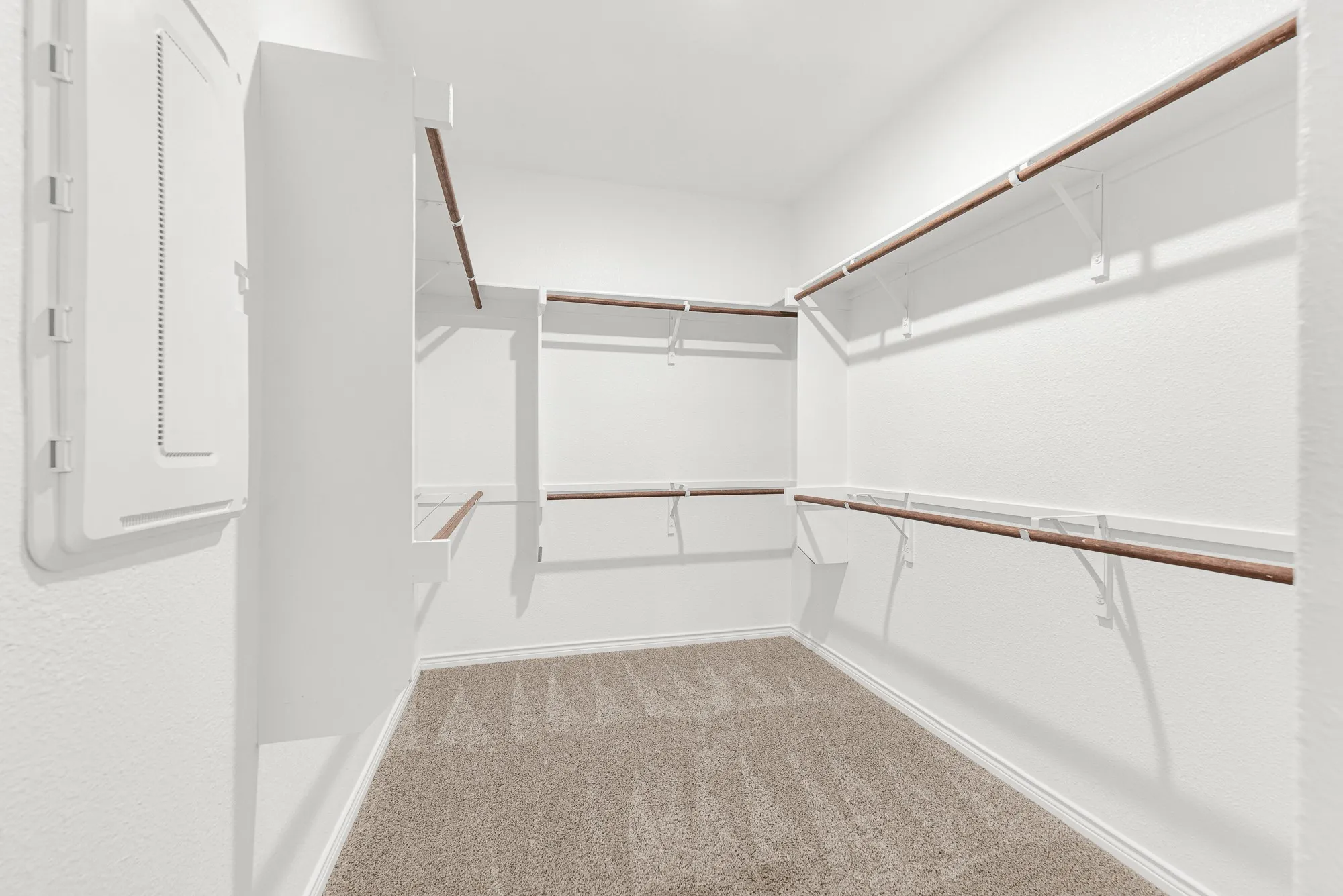 The generous primary closet is fully detailed here, showcasing extensive, multi-level hanging rods and built-in shelving across its carpeted floor. Stay organized effortlessly with this massive storage space that easily accommodates clothing, shoes, and all your storage needs.