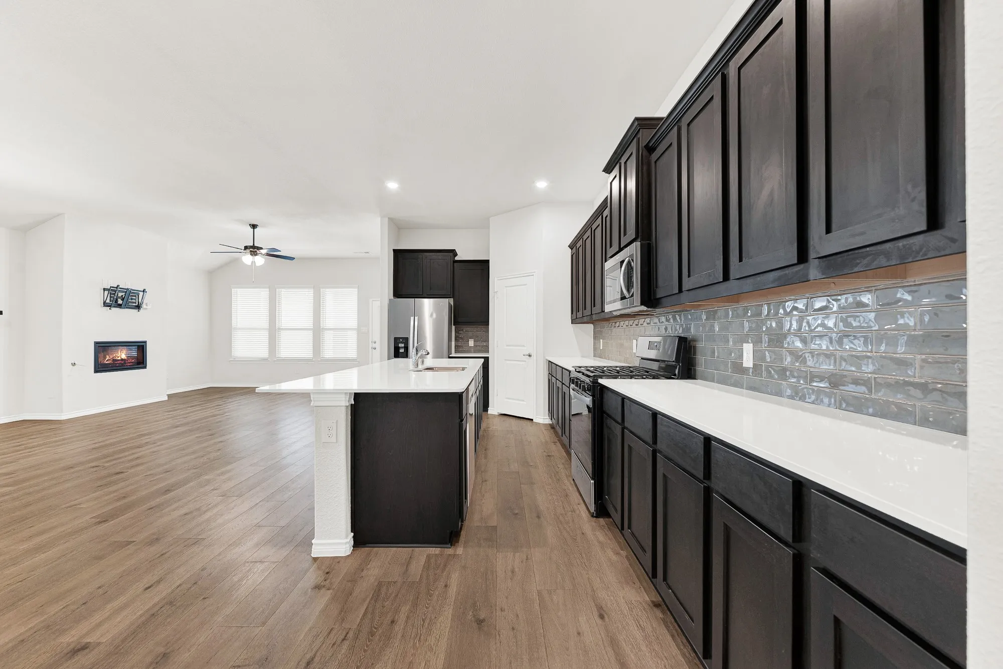 This wide perspective highlights the rich espresso cabinetry and the unique gray subway tile backsplash that runs the length of the kitchen counter. Preparing dinner feels efficient and organized when you have this much counter space and such sleek surfaces.