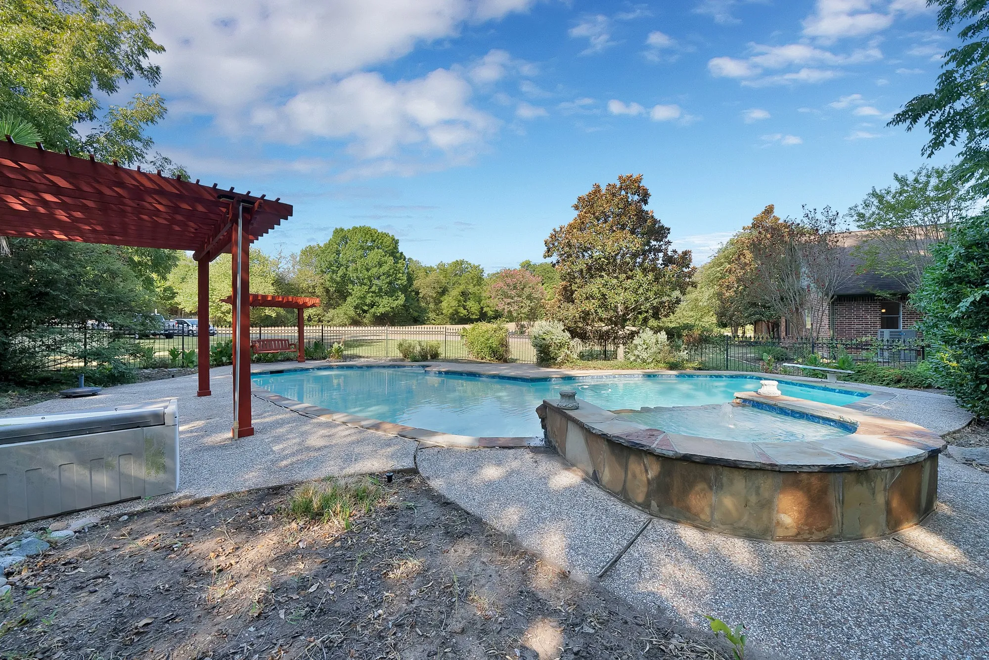 Outdoor swimming pool with integrated spa and stone surround, concrete decking, and a red wood pergola