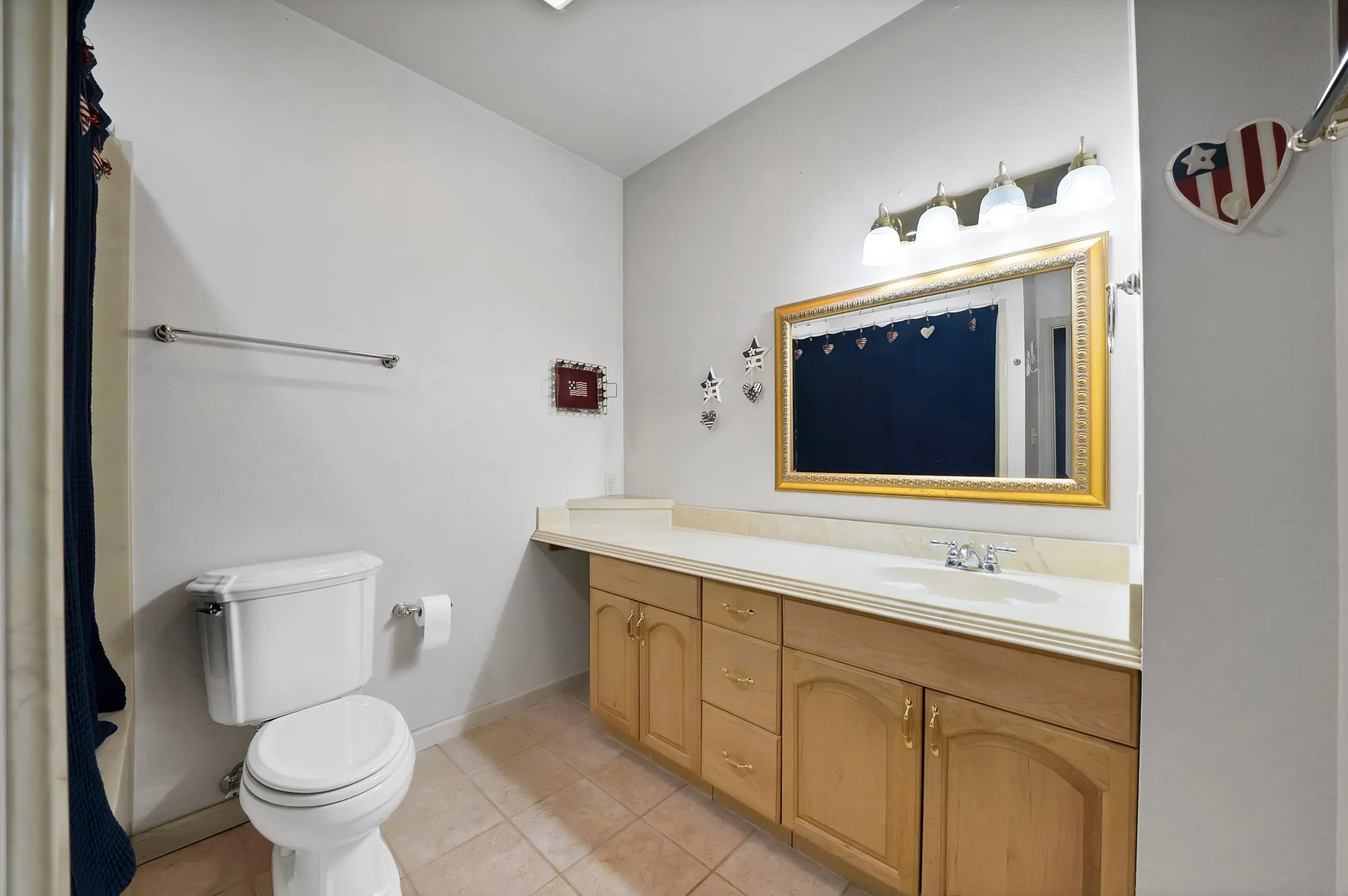 Recessed ceiling lighting, full vanity with integrated sink, gold-framed mirror, and tiled flooring. Bath/shower combo.