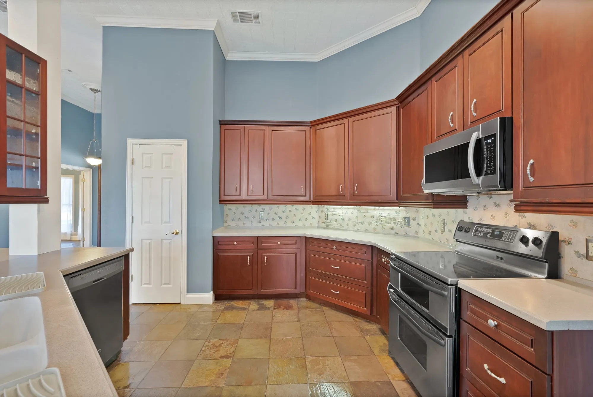 Wood cabinetry with brushed nickel hardware, stainless steel appliances, light-toned countertops, decorative backsplash, and tiled flooring
