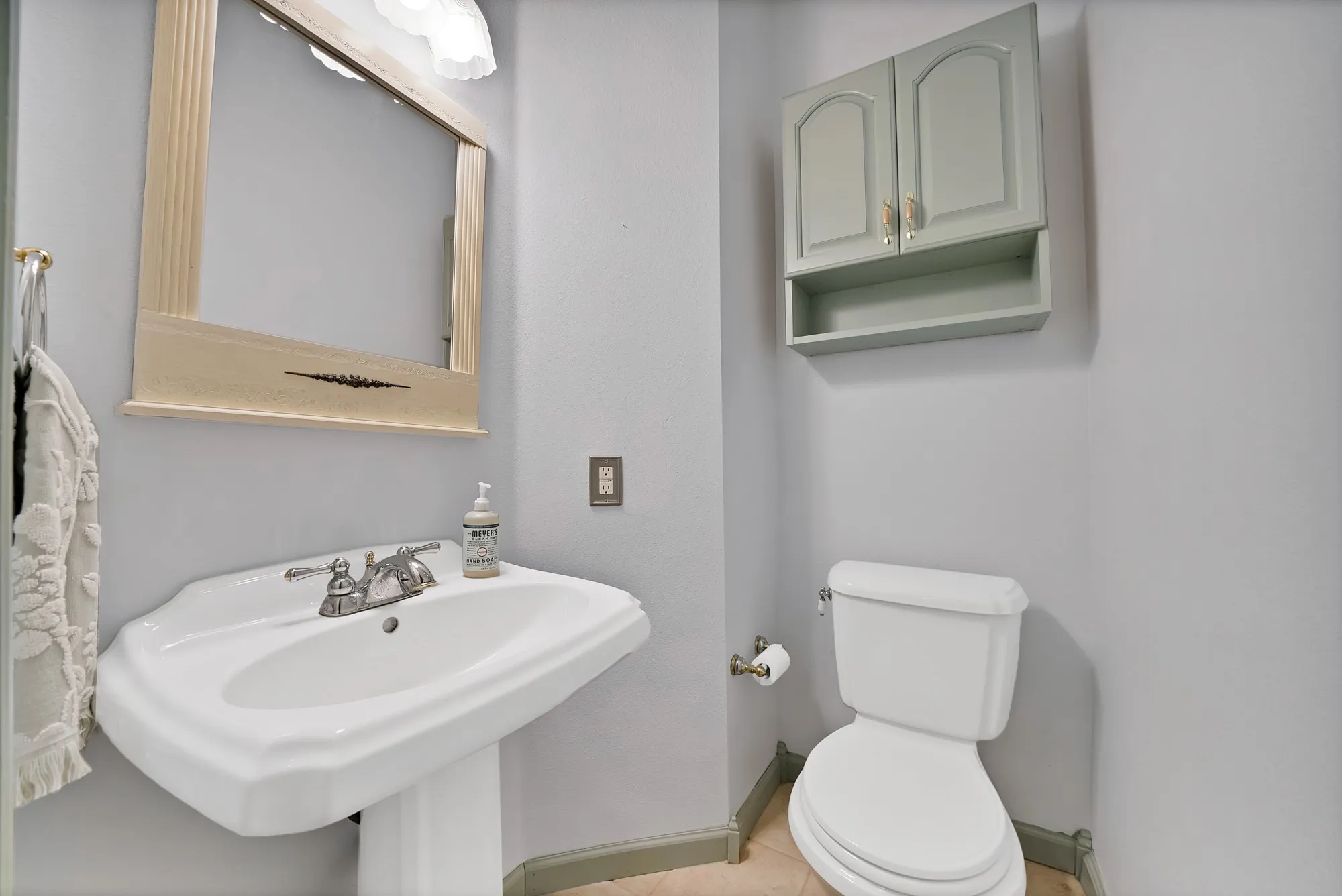Pedestal sink with chrome faucet, toilet, wall-mounted storage cabinet, and vanity mirror with integrated lighting
