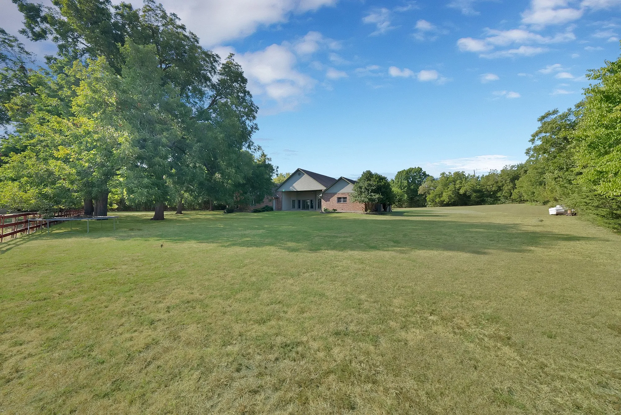 Expansive lawn with mature trees and a wood-fenced perimeter