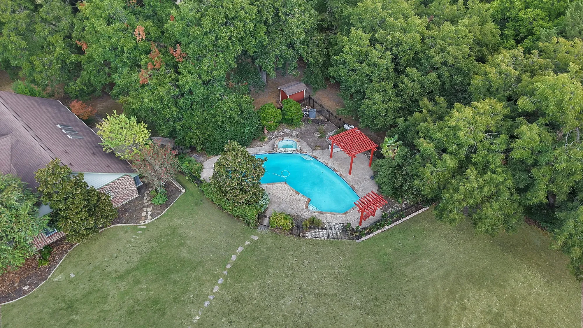 Landscaped backyard featuring a swimming pool with integrated spa, stone coping, and red pergolas