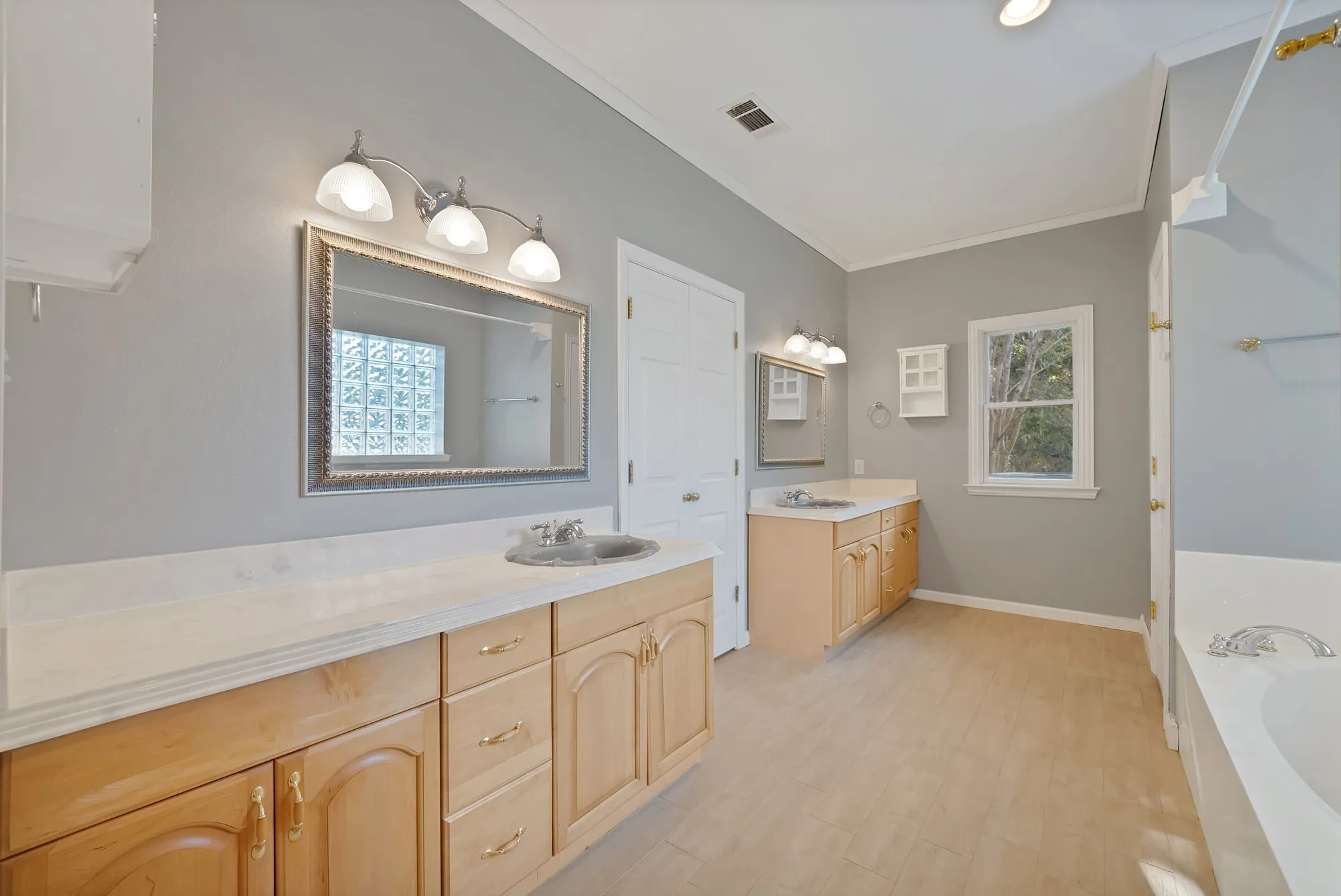 Dual vanity sinks, light wood-finish cabinetry, light-colored countertops, large framed mirrors, and a built-in tub